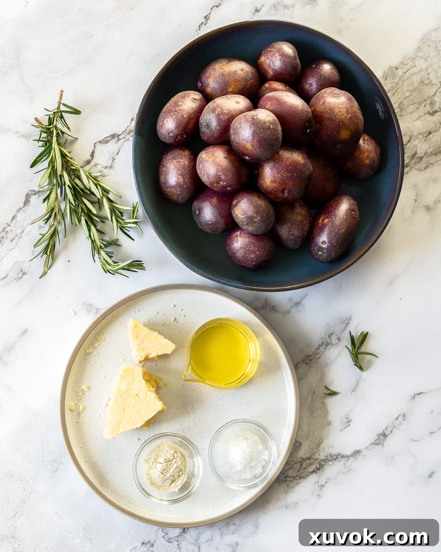A flat lay of ingredients for parmesan smashed potatoes including baby potatoes, rosemary, parmesan, and oil.