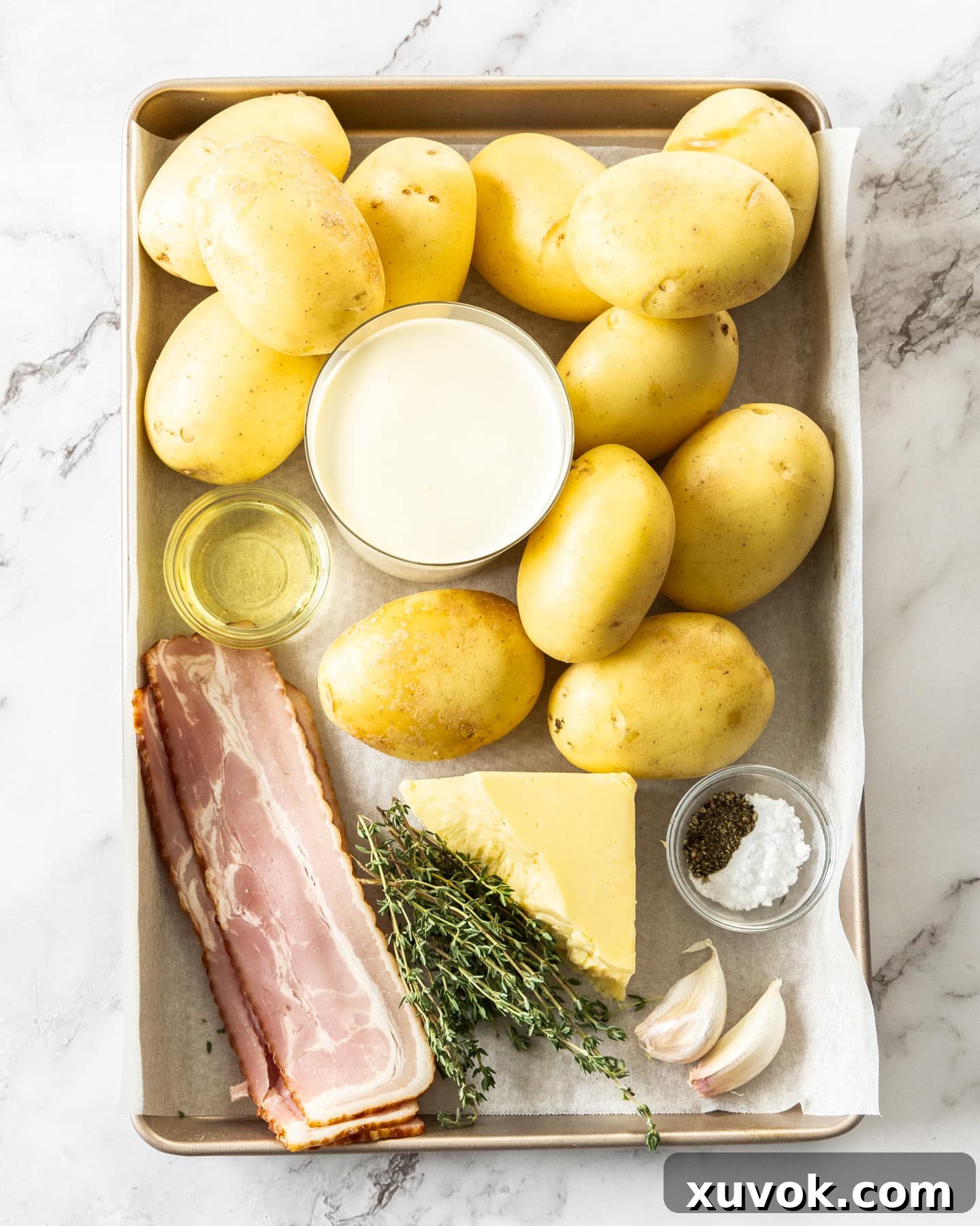 Ingredients for hasselback potato gratin on a baking tray, showcasing fresh and essential components.