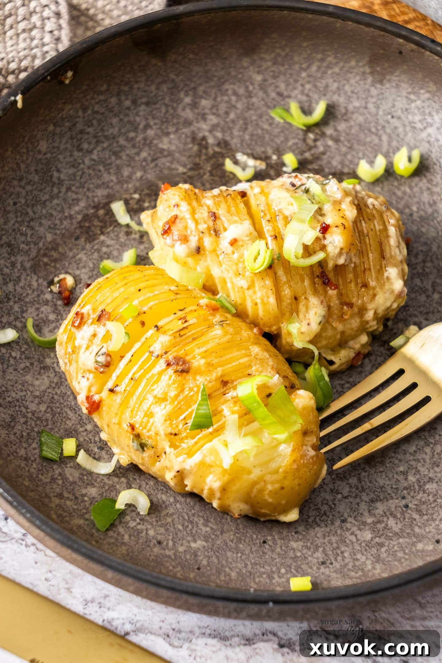 Two hasselback potatoes on a plate, ready to be served, showcasing their fanned appearance.