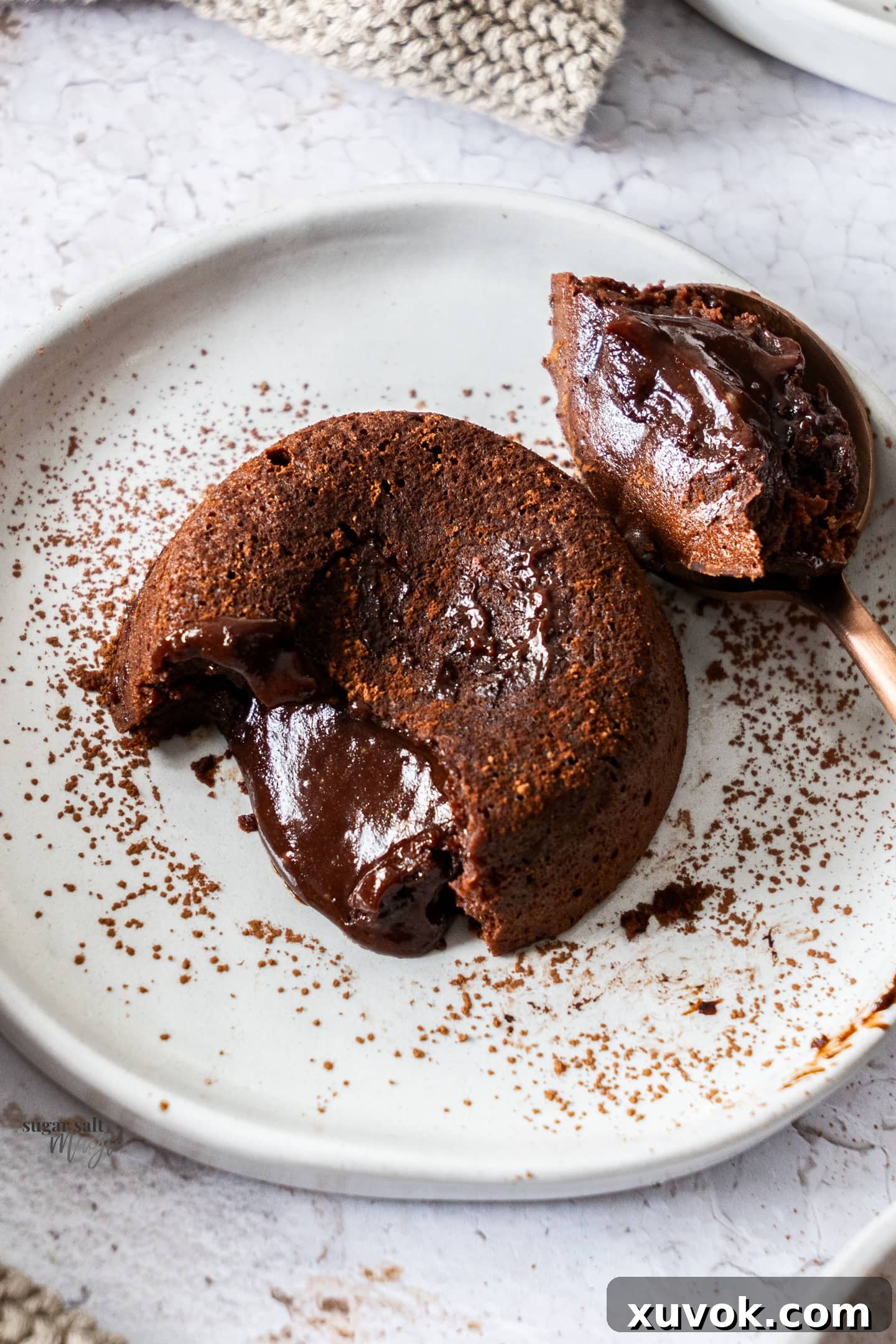 A top-down view of a chocolate fondant on a plate, with a spoon having just pierced it, causing the rich, gooey filling to beautifully ooze out.