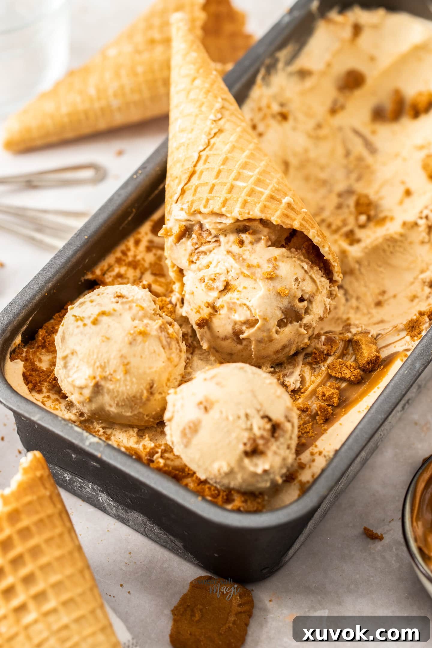 Scoops of cookie butter ice cream, with one perfectly placed in a waffle cone.