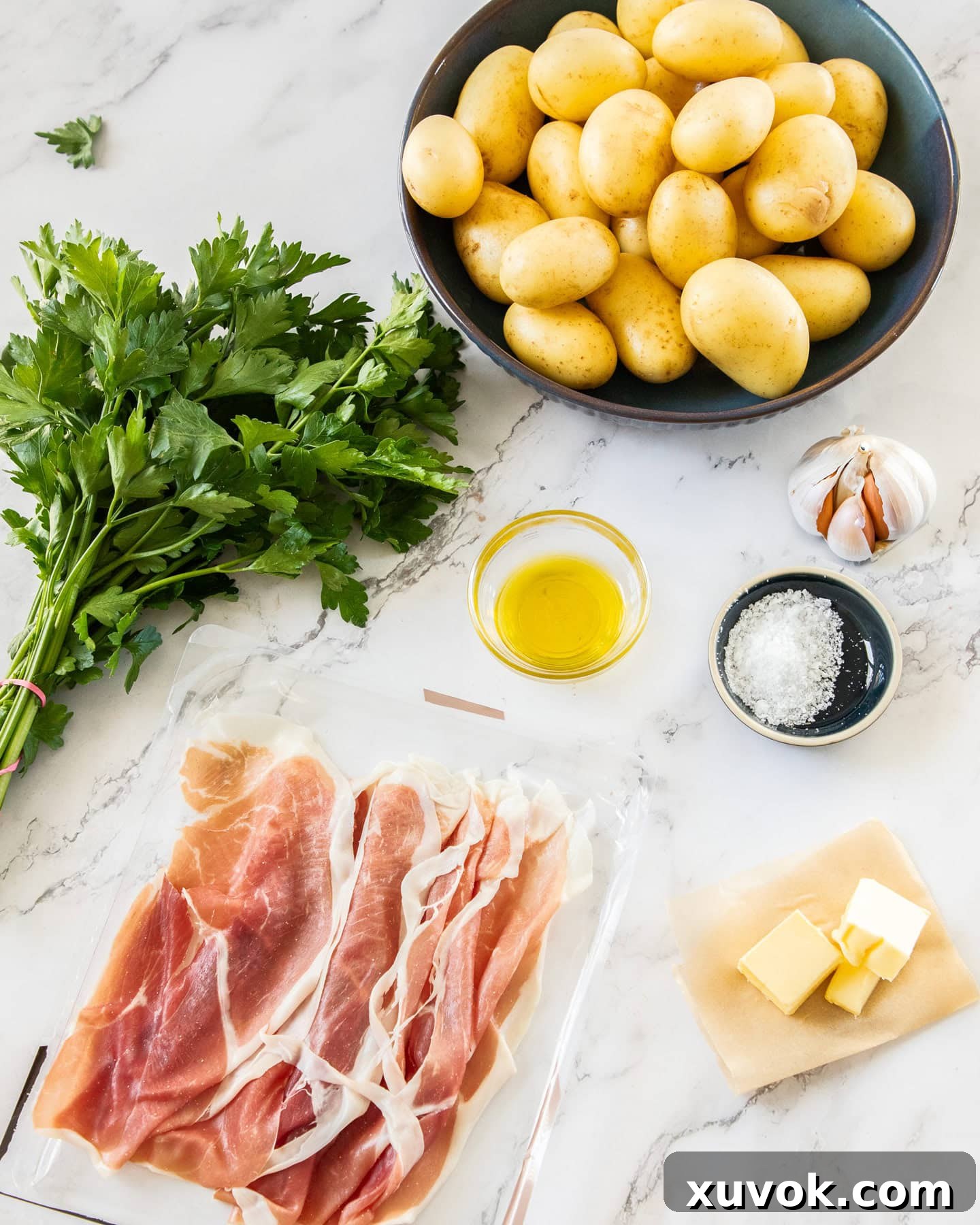 A beautiful flat lay of fresh ingredients for garlic butter potatoes, including baby potatoes, prosciutto, garlic, butter, and parsley, ready for cooking.