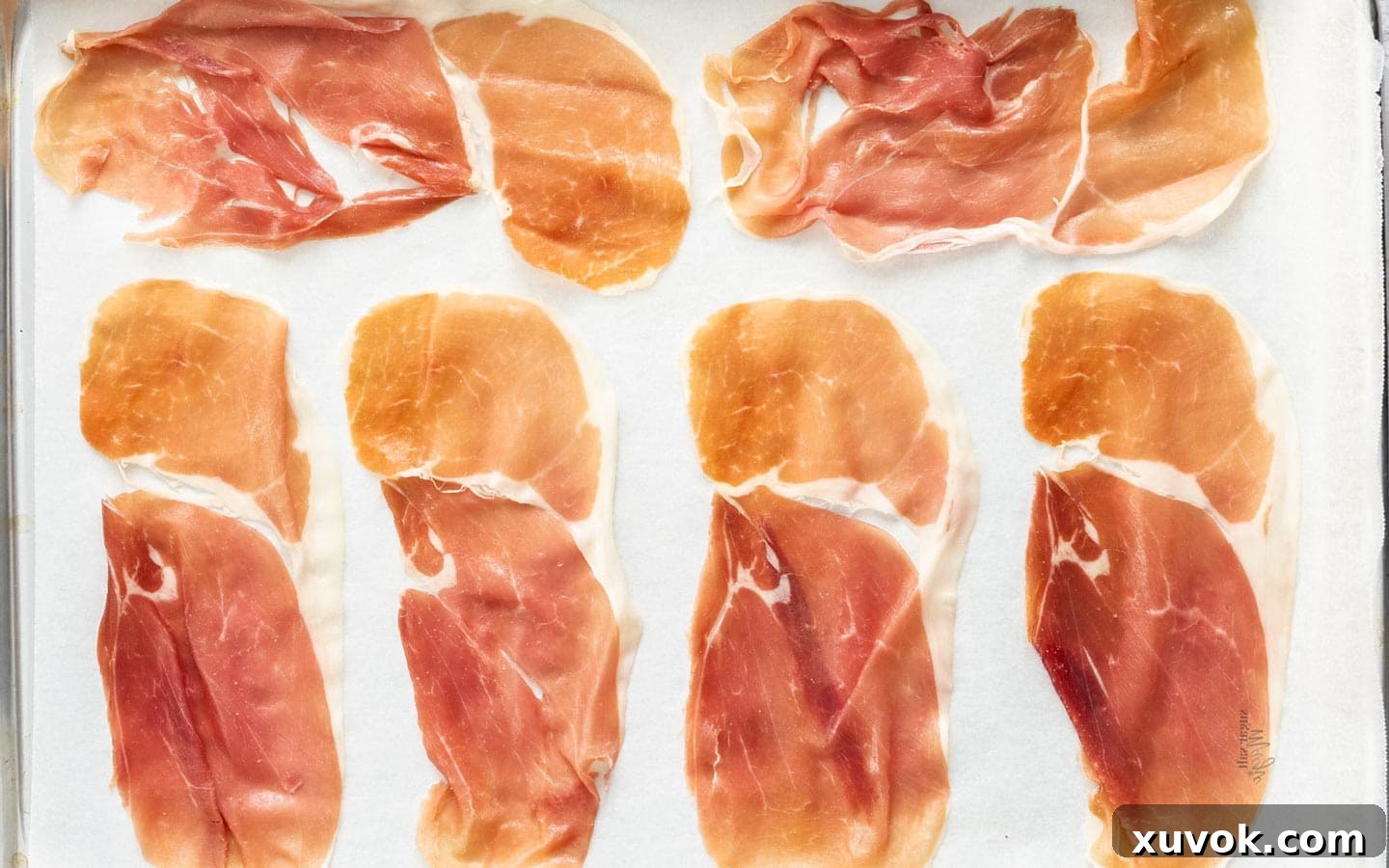 Thin slices of raw prosciutto laid out evenly on a parchment-lined baking sheet, ready for crisping in the oven.
