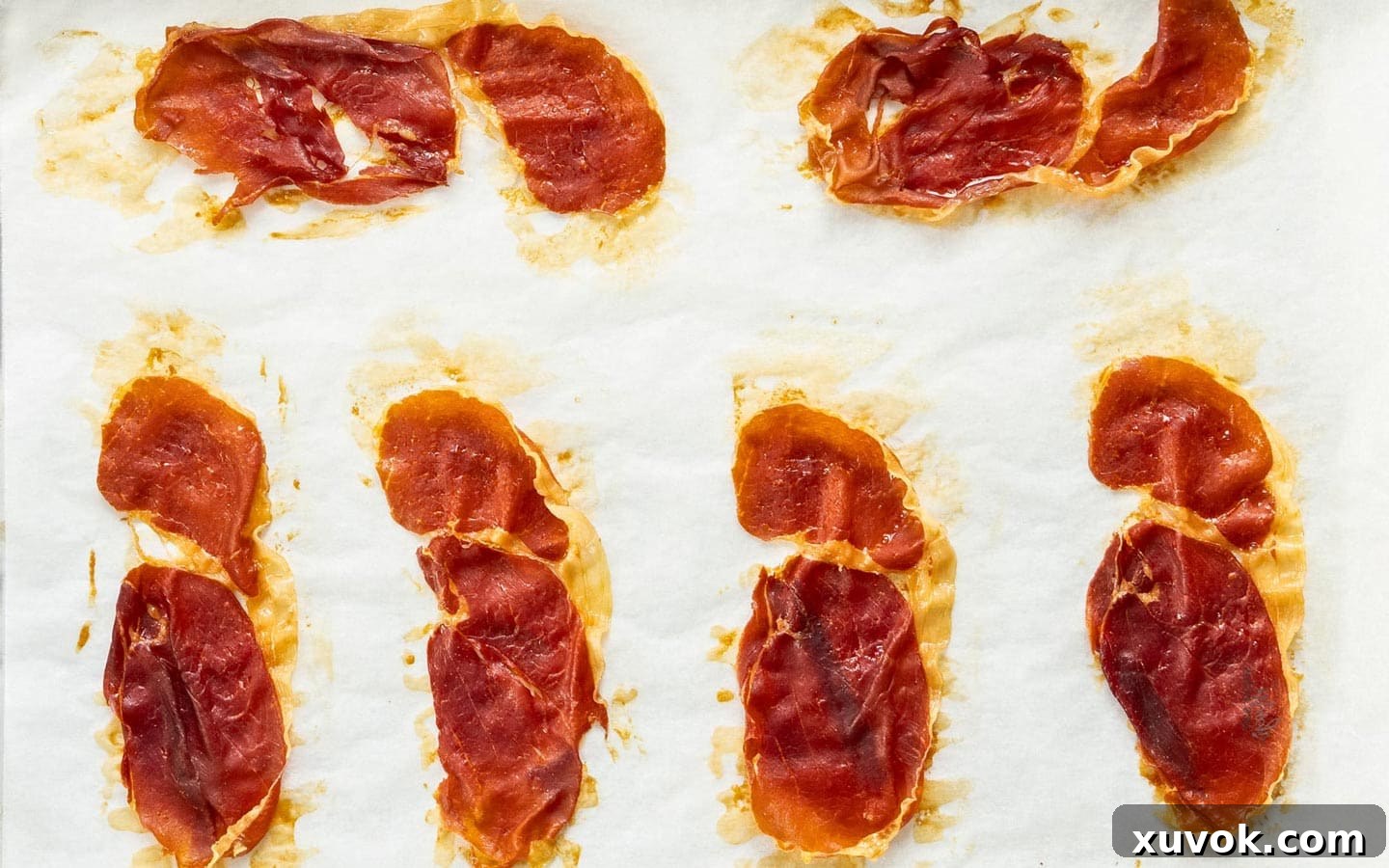 Beautifully crispy prosciutto, golden brown and perfectly rendered, resting on a baking sheet after being cooked in the oven.