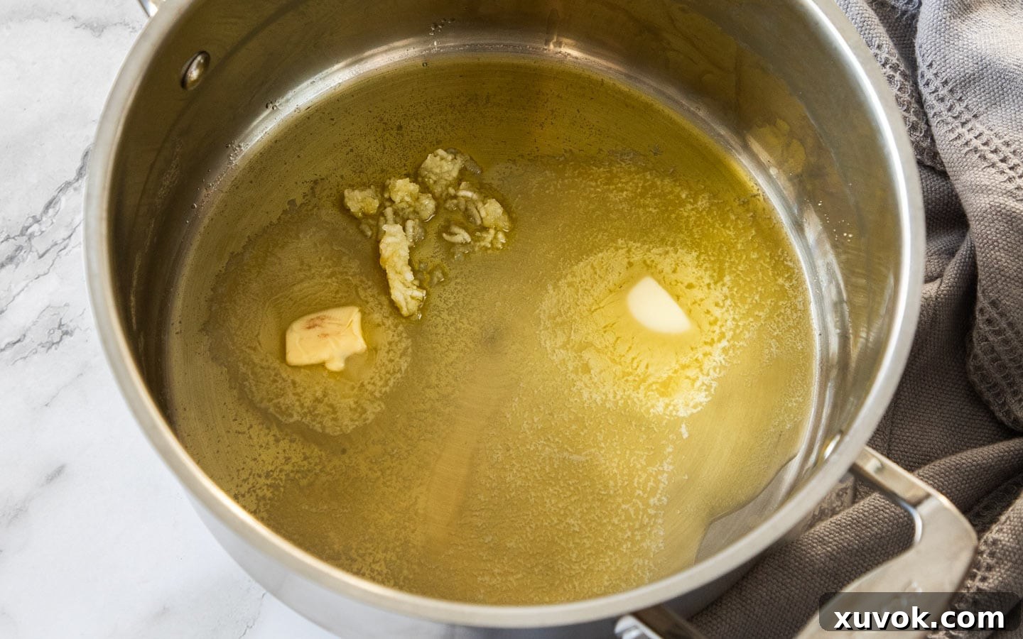 Melted butter and minced garlic sizzling gently in a saucepan over medium heat, creating an aromatic base for the potatoes.
