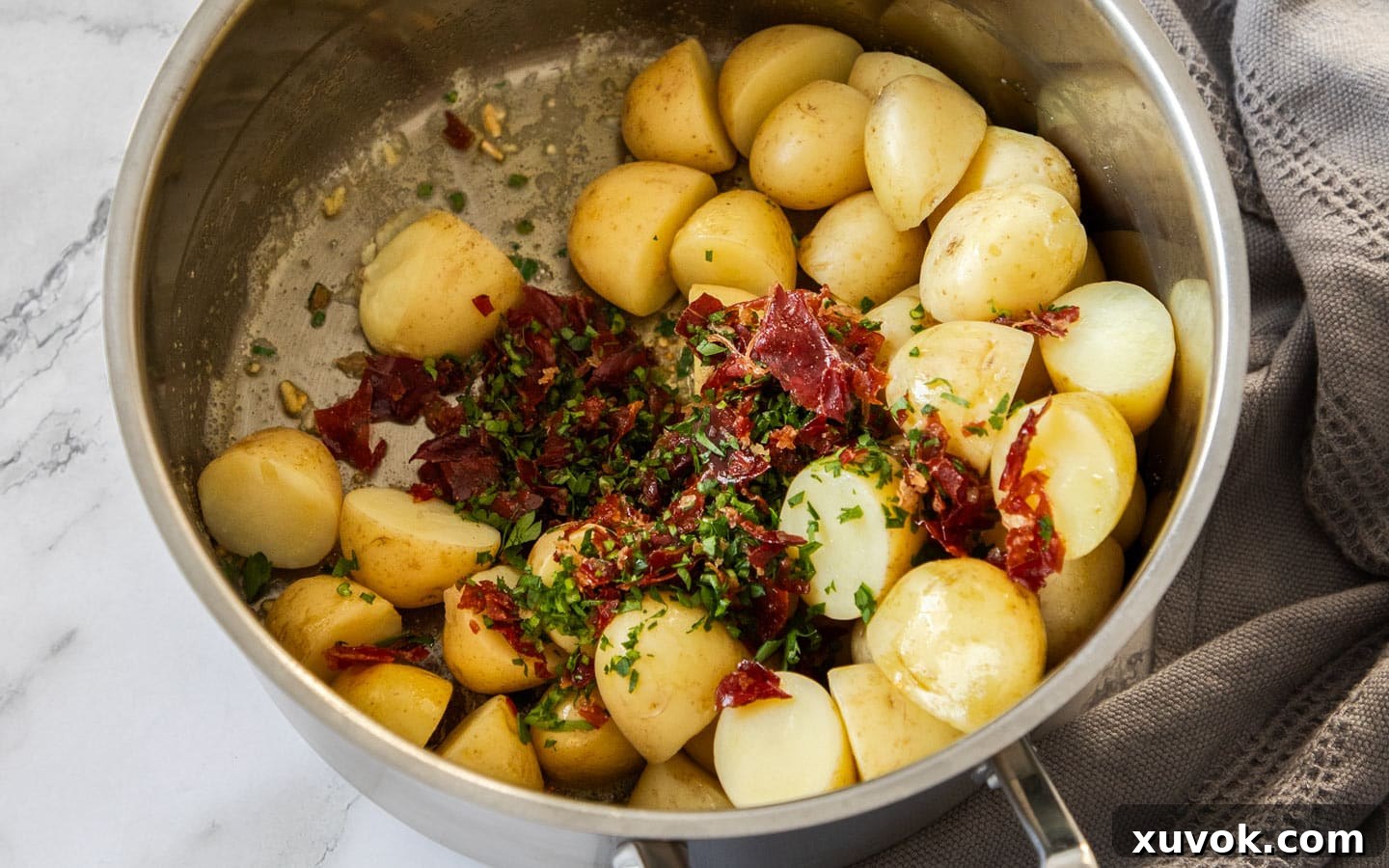 Cooked baby potatoes returned to the saucepan, glistening with butter, ready to be mixed with fresh parsley and crumbled crispy prosciutto.