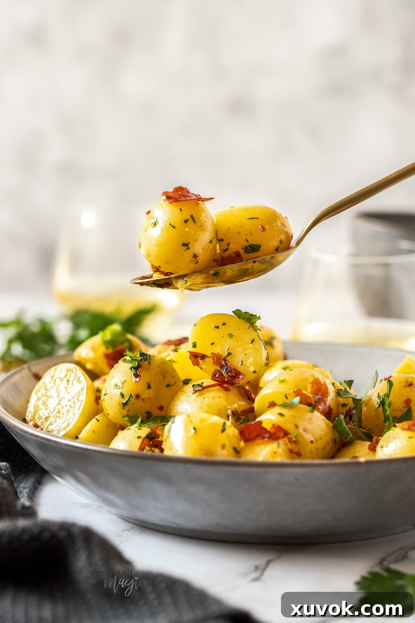A beautifully presented grey bowl brimming with cooked garlic butter potatoes, sprinkled with fresh parsley and crispy prosciutto. A golden serving spoon hovers, poised to scoop a portion.