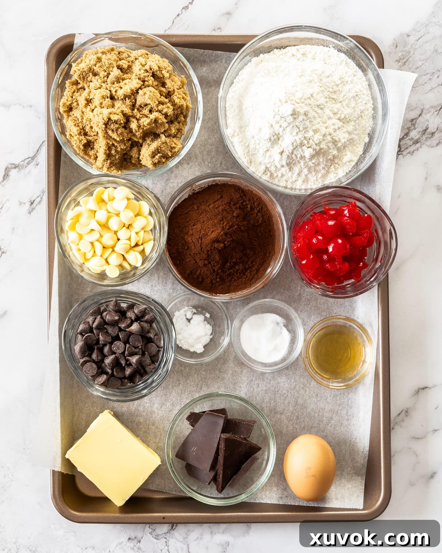 A vibrant selection of ingredients for black forest cookies on a rustic baking tray, featuring dark chocolate, maraschino cherries, butter, and flour.