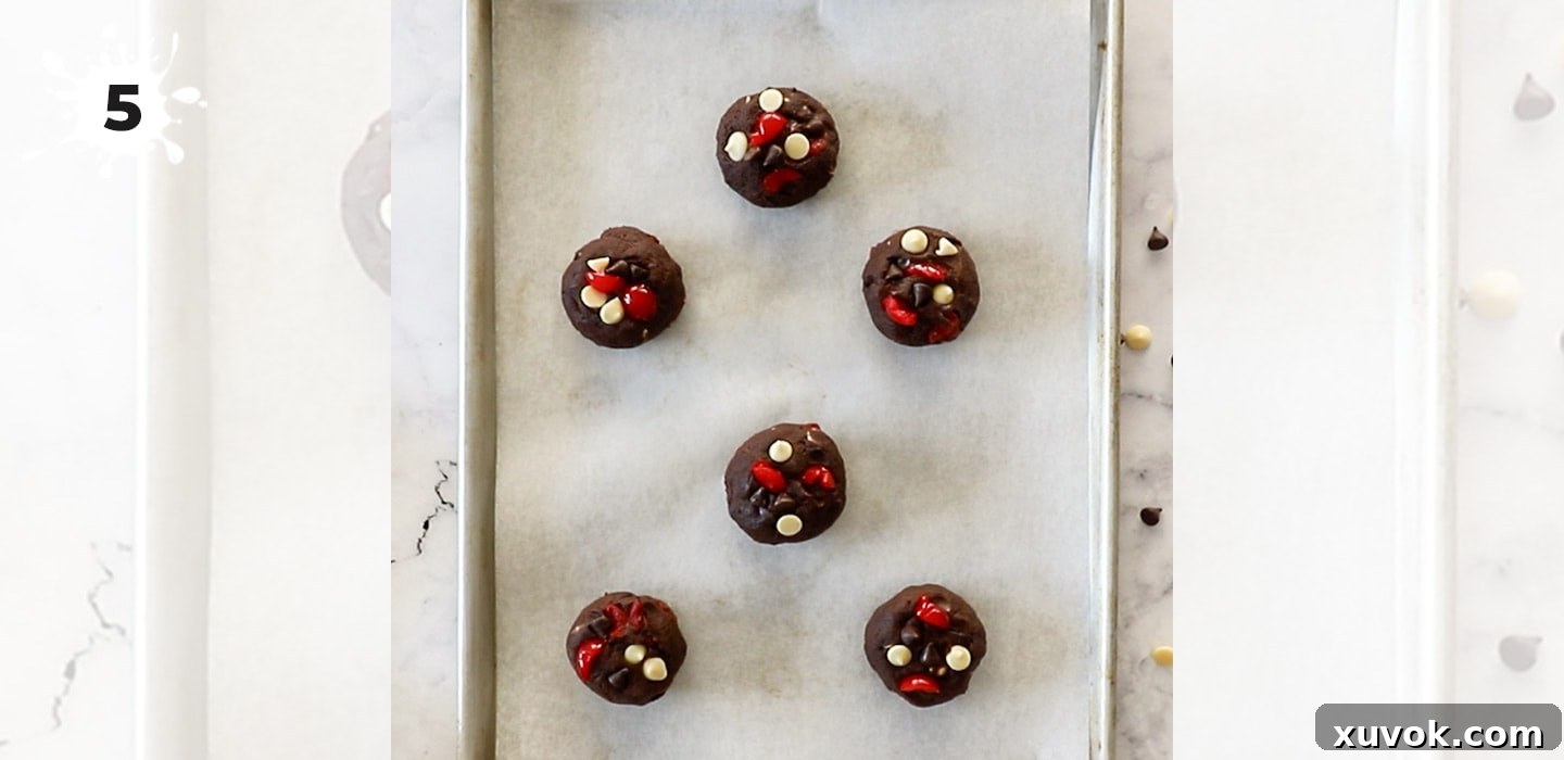 Perfectly rolled balls of Black Forest cookie dough, dotted with chocolate chips and cherries, arranged on a parchment-lined baking sheet, ready for the oven.