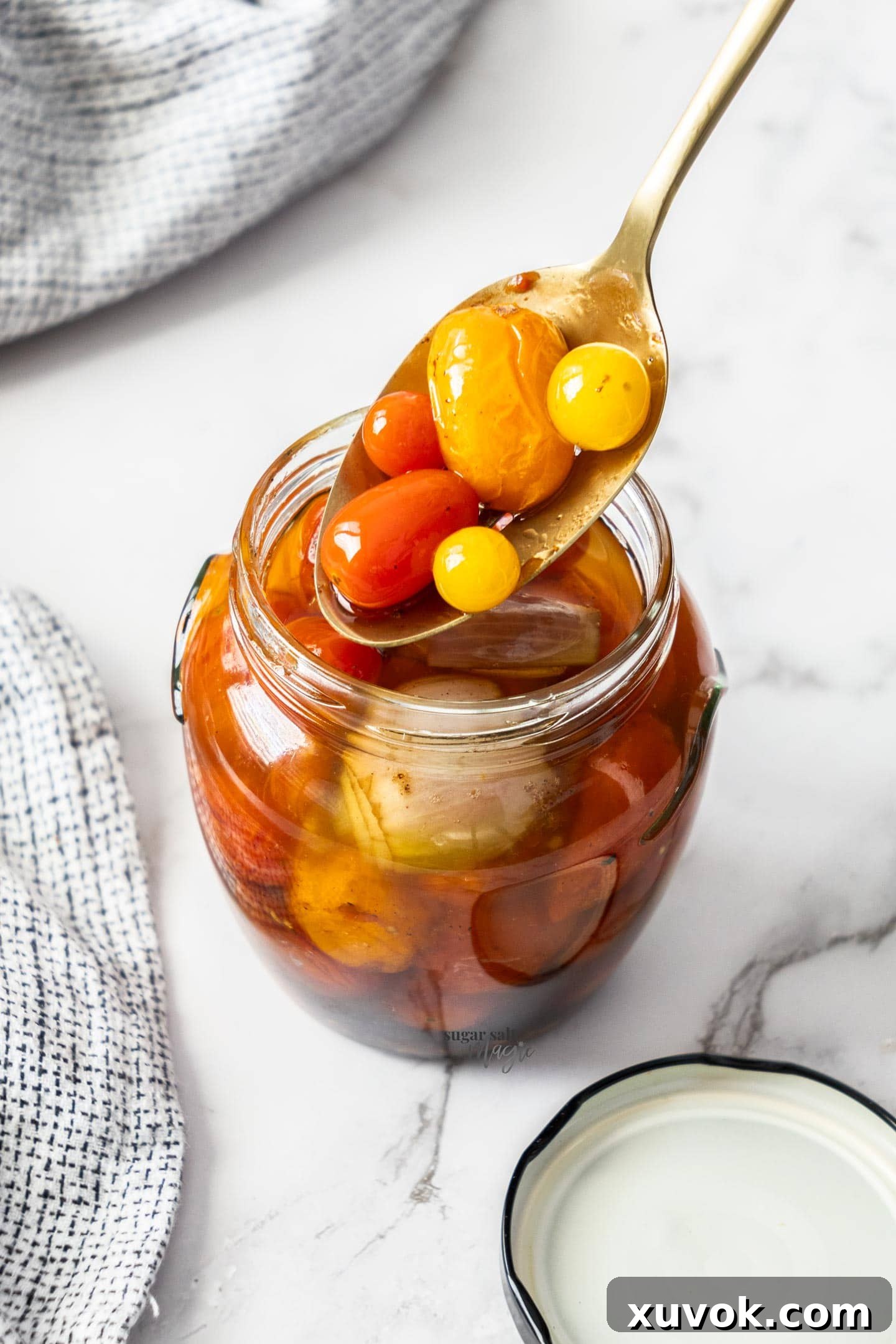 Tomato confit being transferred into a clear glass mason jar, submerged in olive oil, for storage.