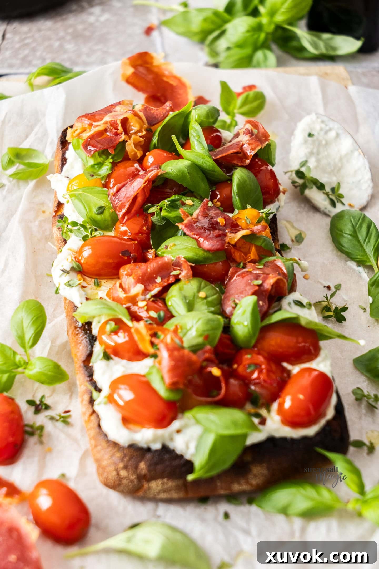 A wide shot of a whole slow roasted tomato bruschetta, beautifully garnished and ready to be served, highlighting the generous toppings of tomatoes, ricotta, and prosciutto on toasted ciabatta.
