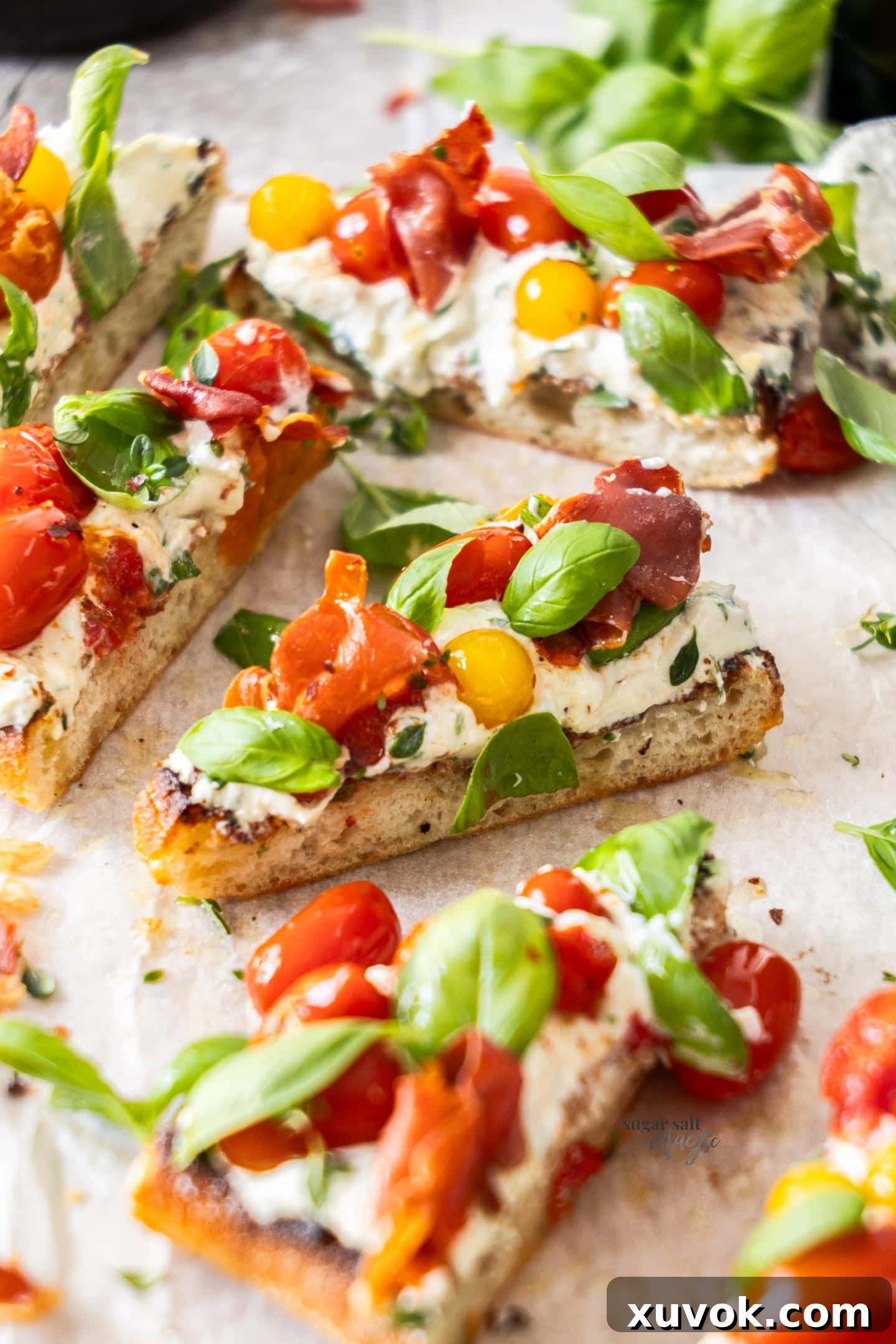 A close-up shot of a single slice of Slow Roasted Tomato Bruschetta, beautifully showcasing the detailed layers of tomato confit, whipped ricotta, basil, and crispy prosciutto.