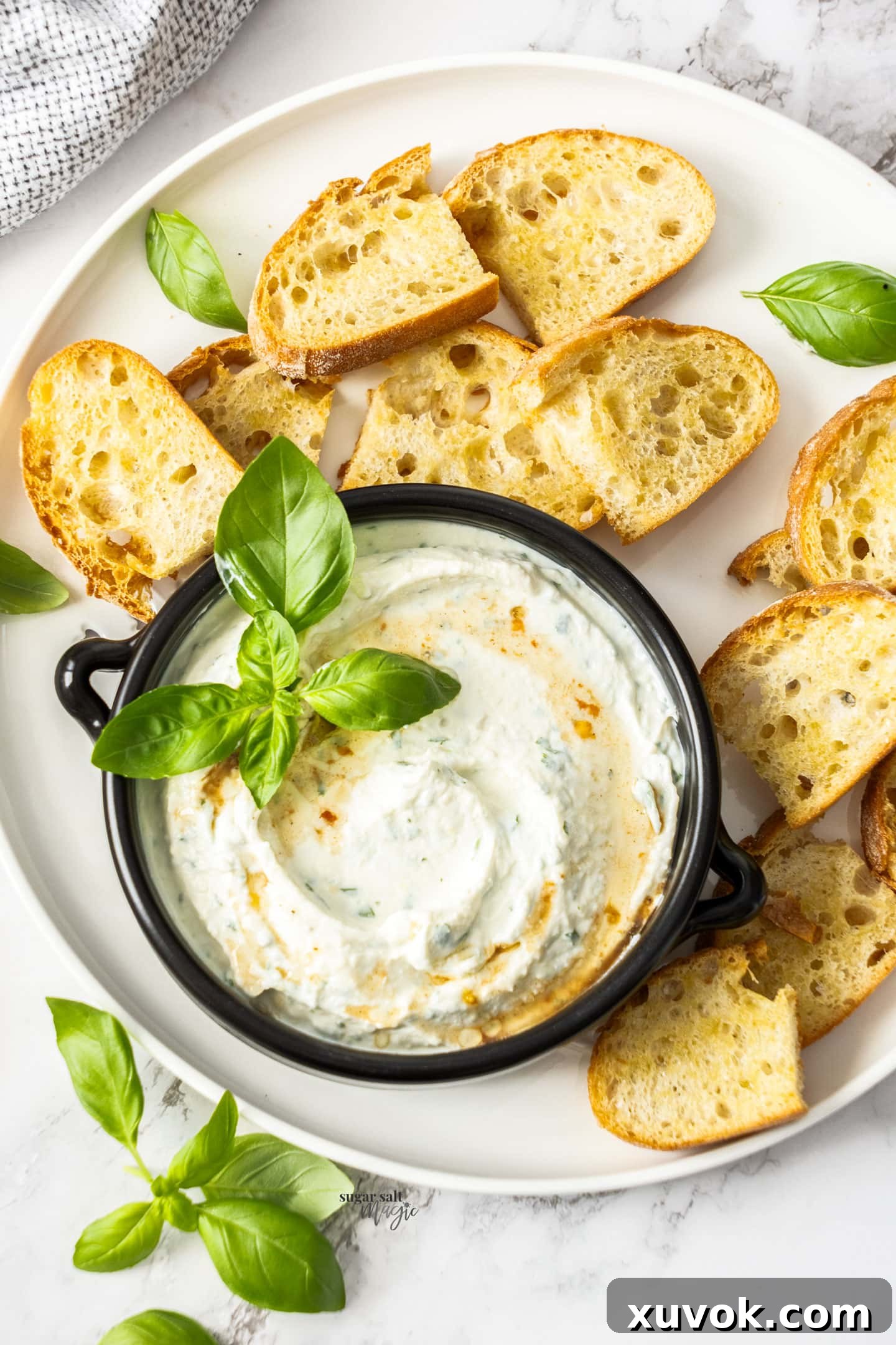 An overhead view of a creamy whipped ricotta dip served in an elegant bowl, garnished with a drizzle of olive oil and fresh basil leaves, showcasing its inviting texture and vibrant presentation. This image captures the delicious appeal of the ready-to-serve appetizer.