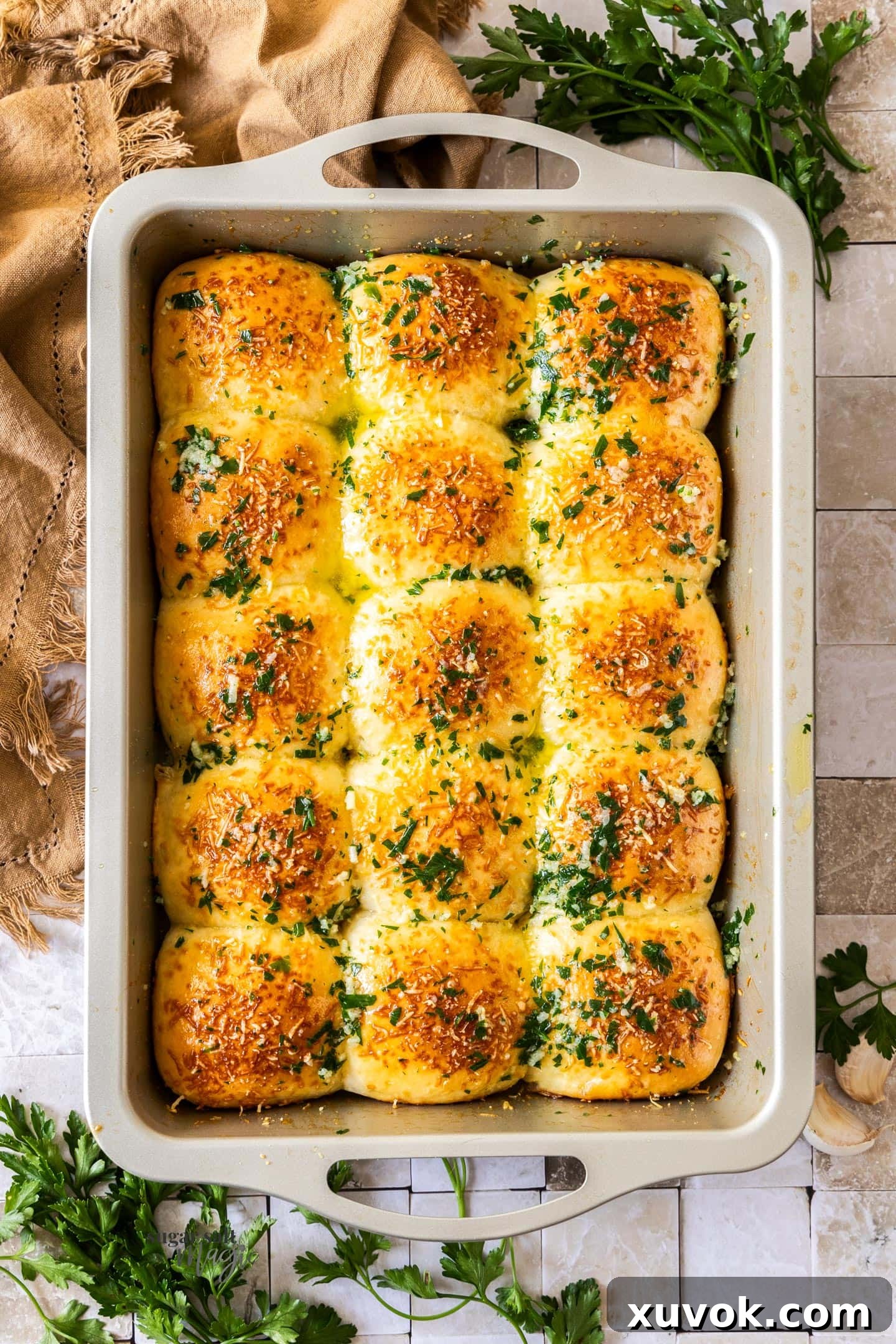 A top-down view of freshly baked garlic dinner rolls, glistening with melted garlic butter and sprinkled with parsley, arranged in a baking dish.