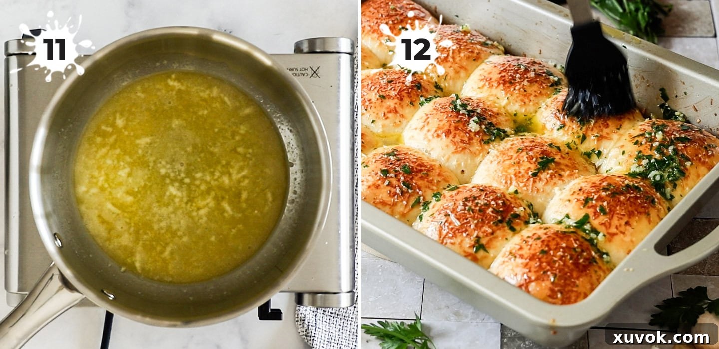 A hand brushing melted garlic butter over the tops of hot, freshly baked dinner rolls in a baking dish.