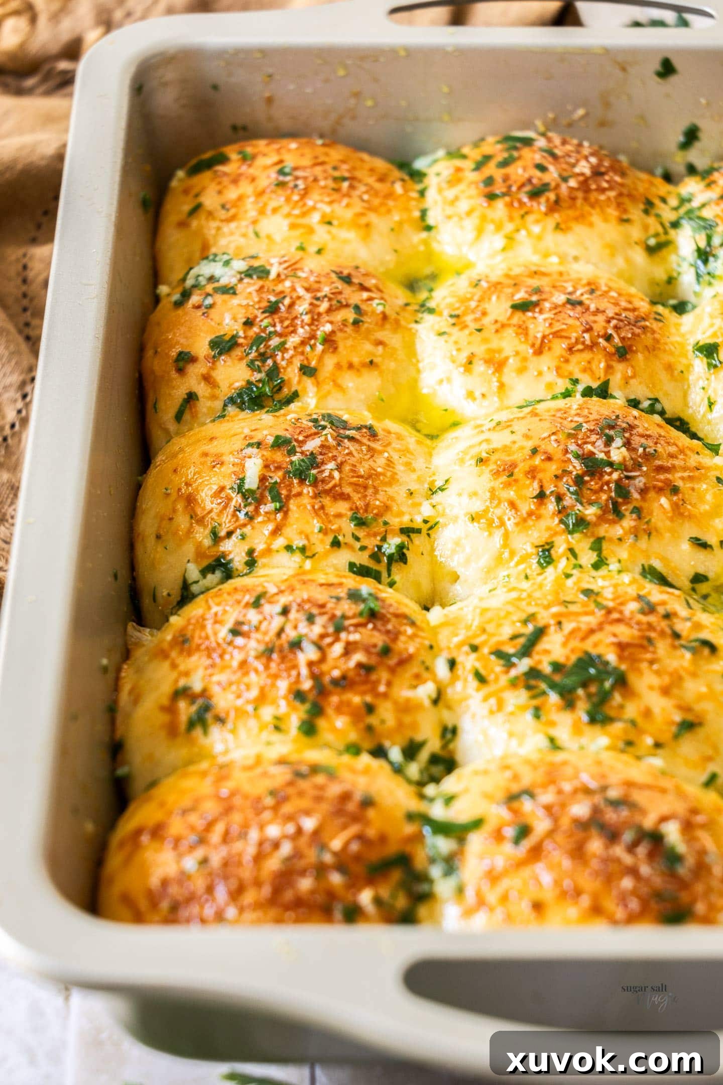 A close-up shot of several garlic dinner rolls, perfectly golden and soft, with a hint of green parsley from the garlic butter, ready to be served.
