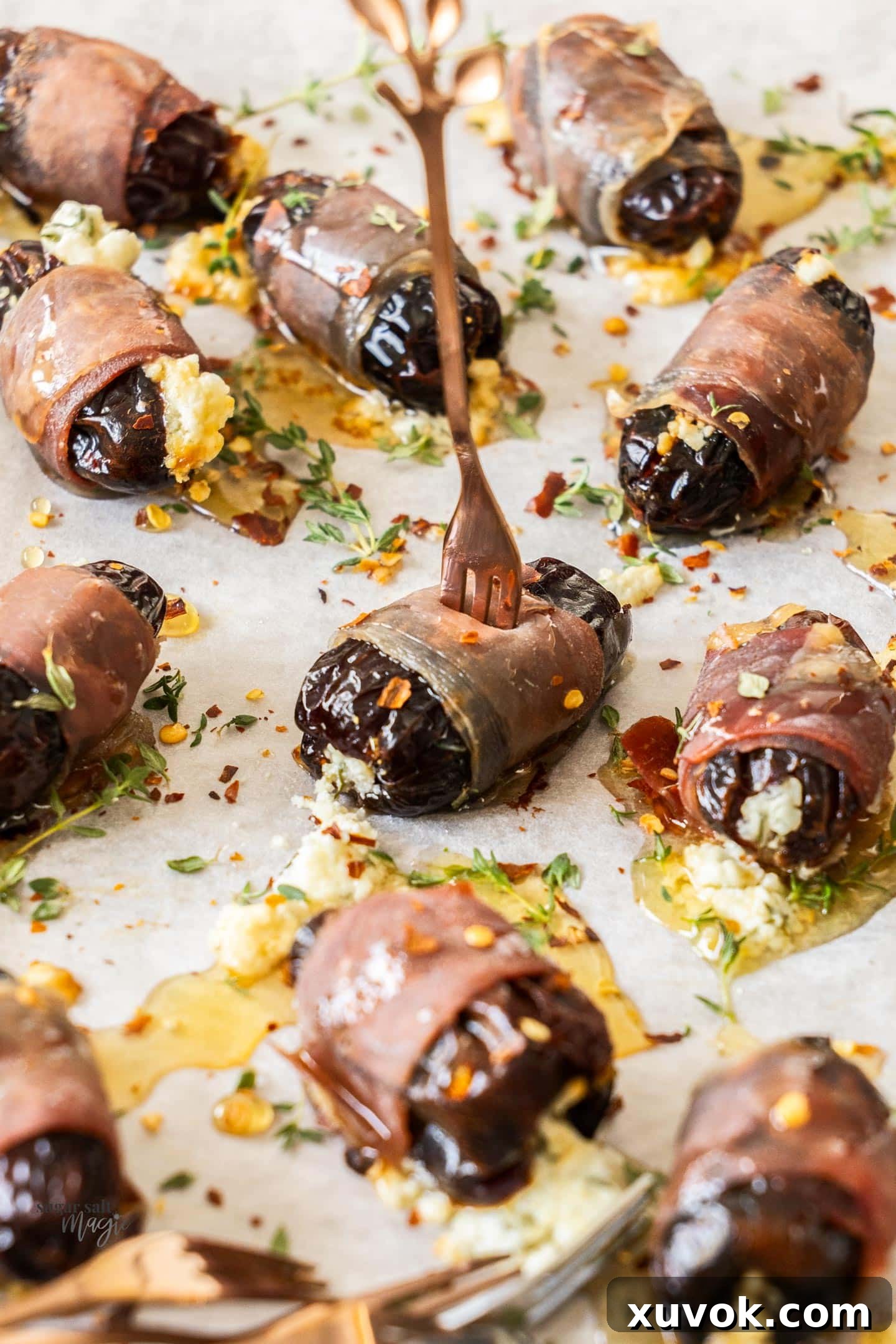 A single prosciutto wrapped date with an appetizer fork stuck into it, ready to be enjoyed.