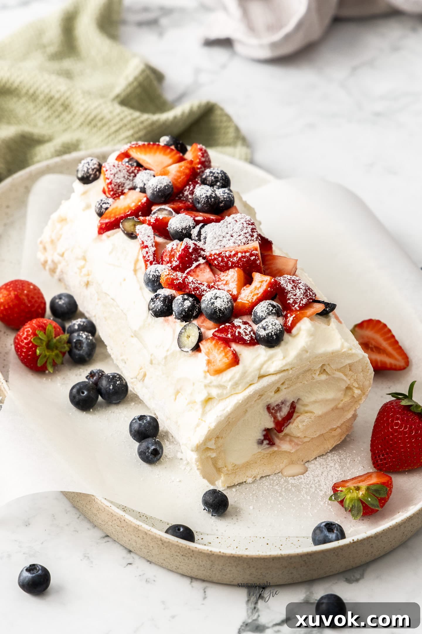 A meringue roulade on a long serving plate, garnished with fresh berries and mint.