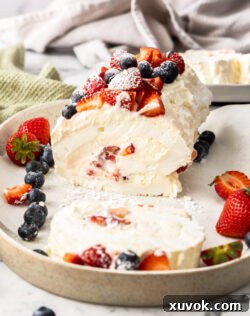 A pavlova roll topped with berries with one slice cut away.