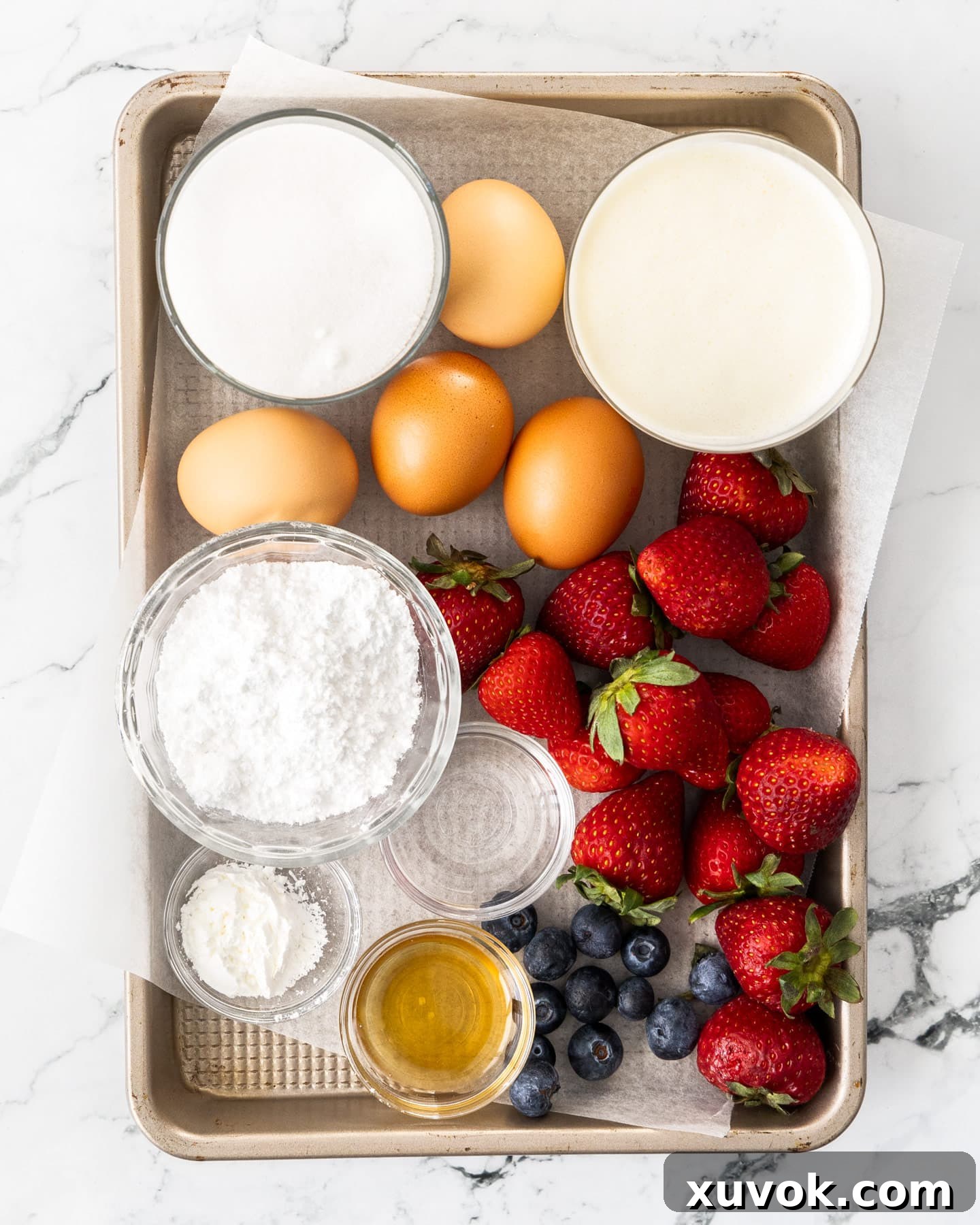 Ingredients for meringue roulade laid out on a baking tray, including eggs, sugar, flour, and berries.