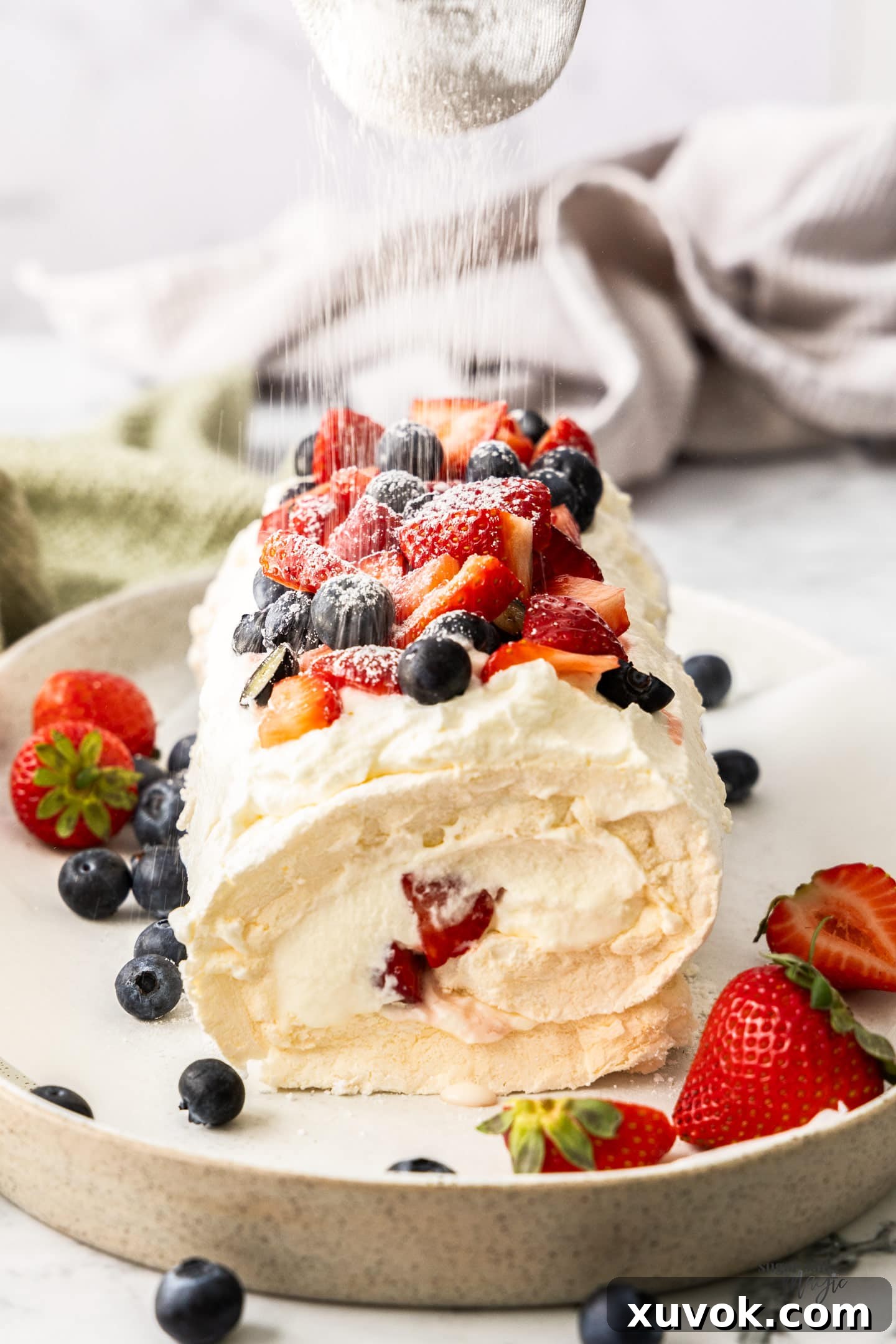 Icing sugar being dusted over the top of the finished pavlova roll, enhancing its aesthetic appeal.