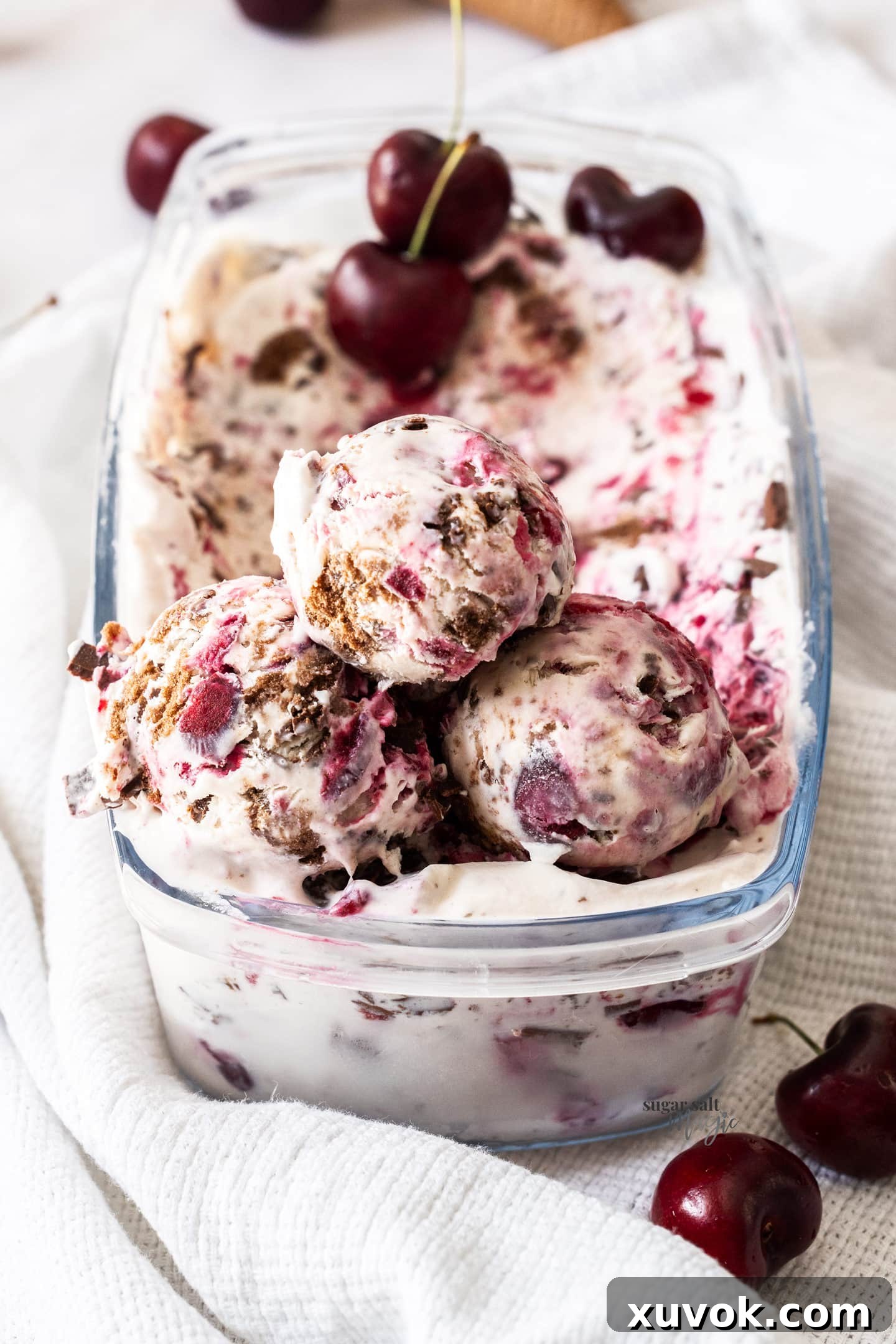 Three generous scoops of Black Forest Ice Cream stacked in an ice cream container, showcasing the rich chocolate and cherry swirls.