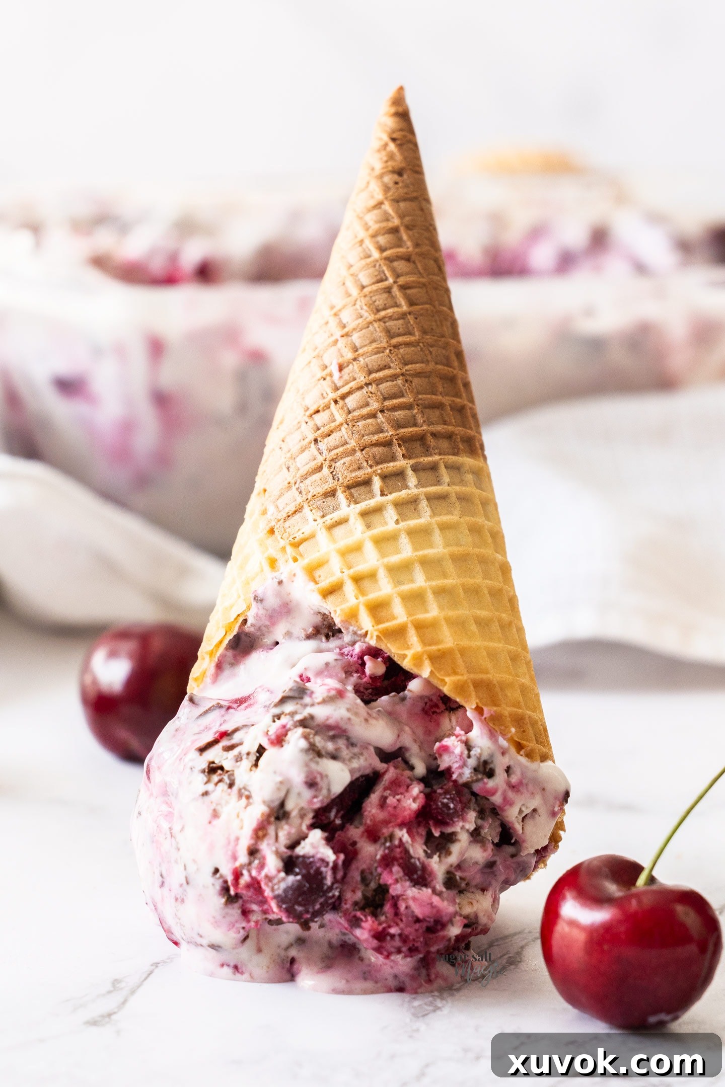 A waffle cone generously filled with Black Forest Ice Cream, inverted and resting on a surface, inviting a delightful bite.