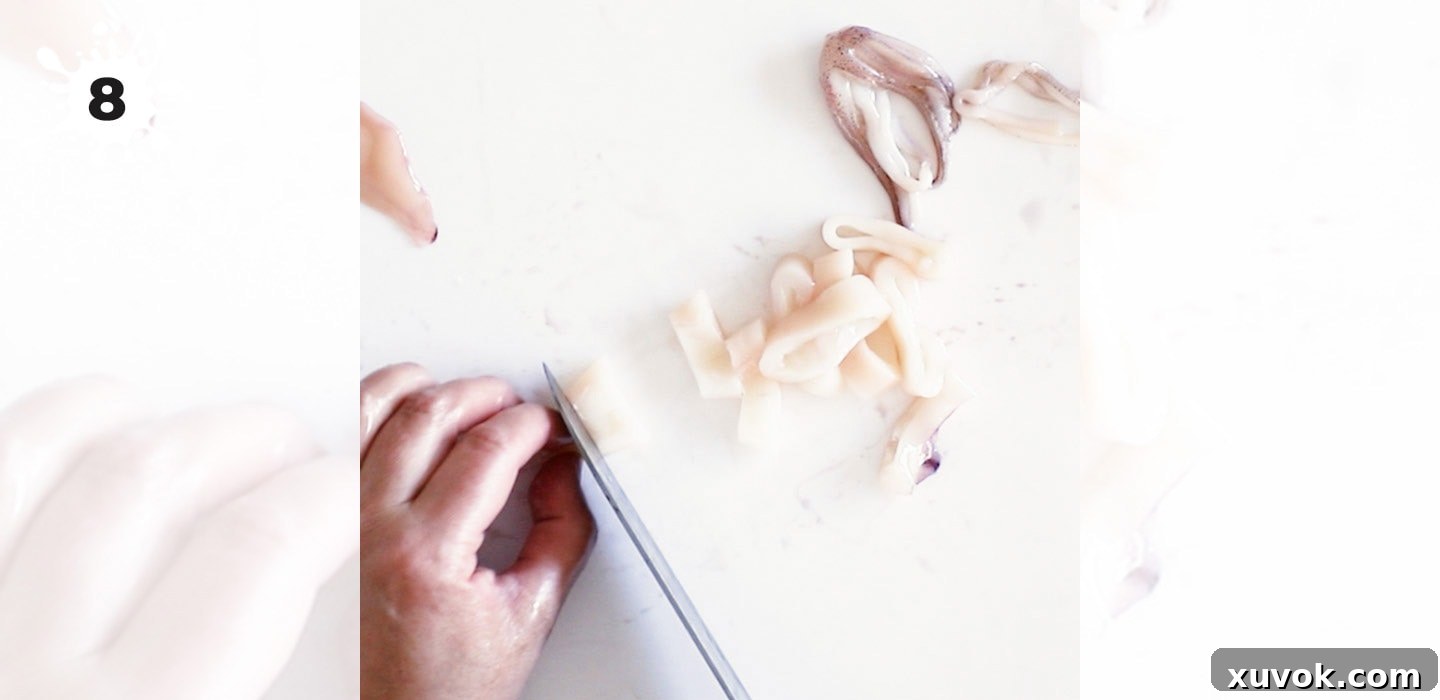 Slicing the cleaned squid mantle into uniform rings on a chopping board.