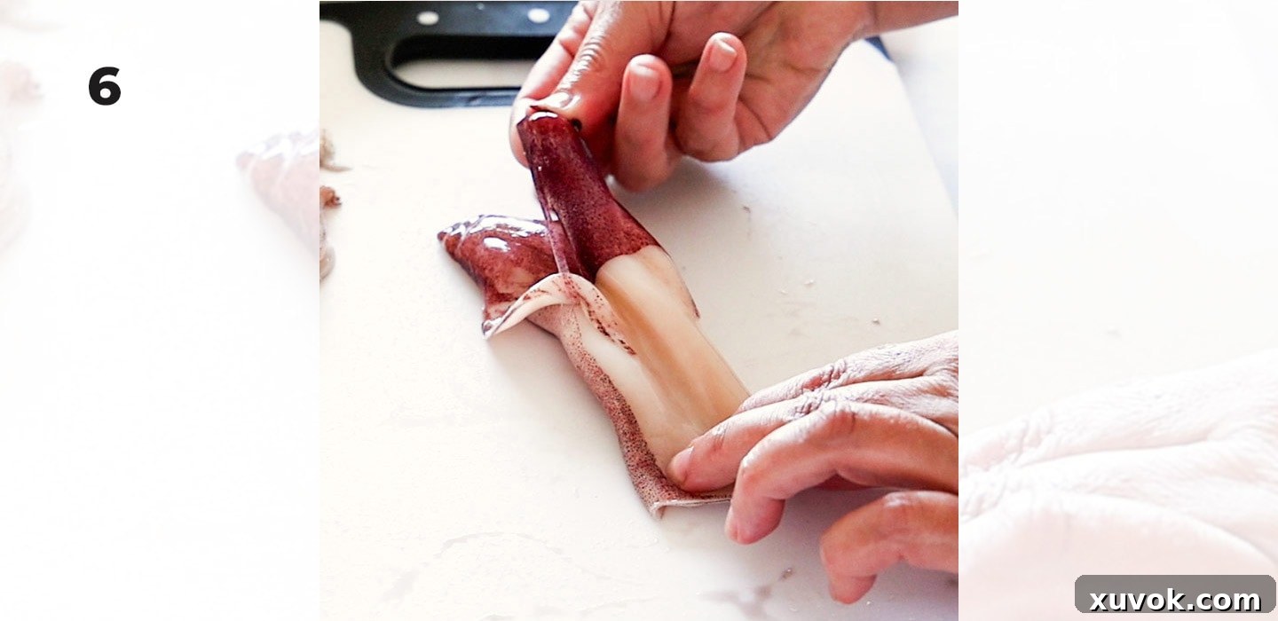Peeling the thin, purple outer skin off the squid mantle to reveal the clean, white flesh.
