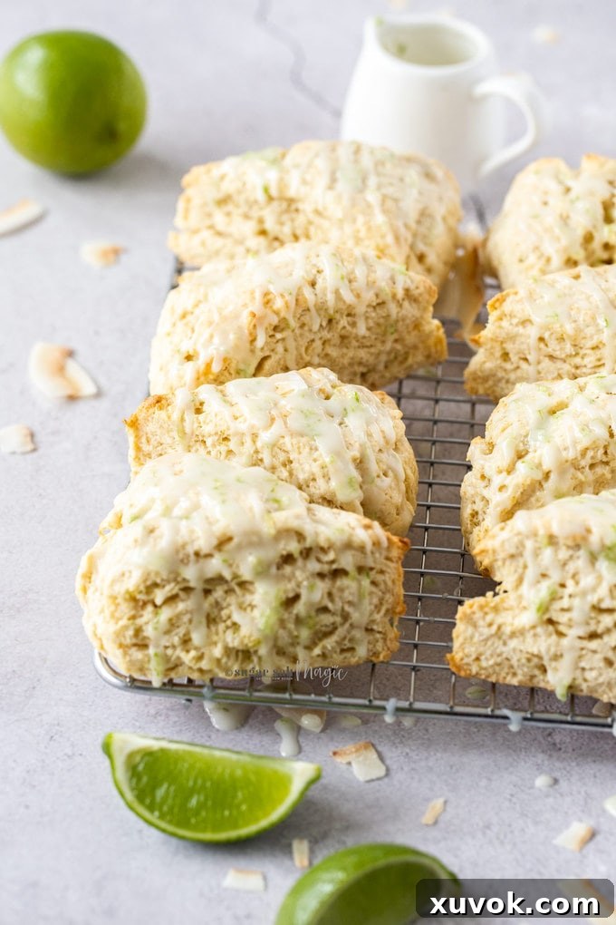 A fresh batch of golden-brown lime coconut scones cooling on a wire rack, with vibrant green lime wedges scattered around for garnish. The scones exhibit a perfectly crisp exterior with visible cracks, hinting at their tender interior, inviting you to enjoy this tropical morning or afternoon tea treat.