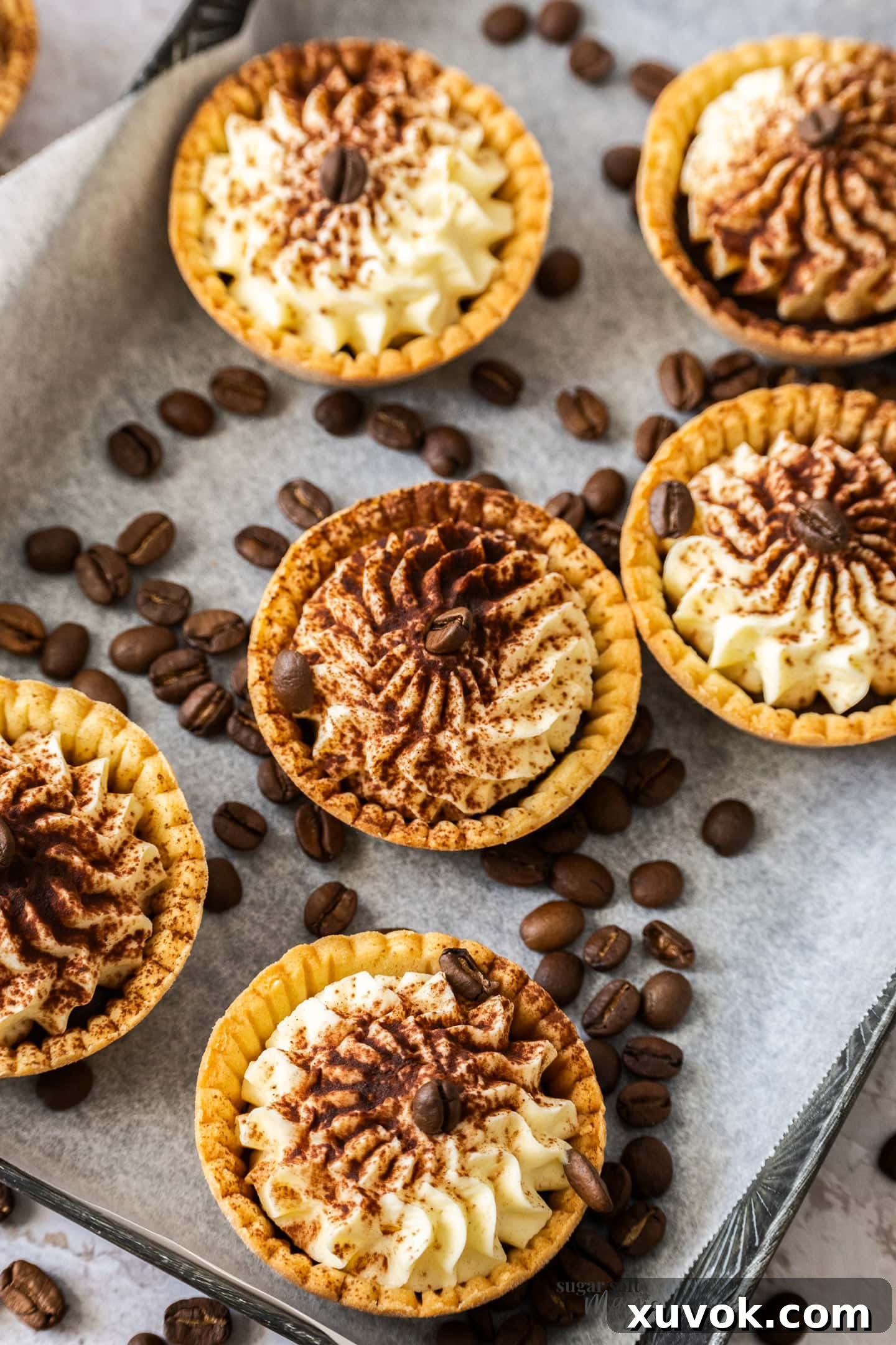 6 cream filled tartlets on a metal tray surrounded by coffee beans.