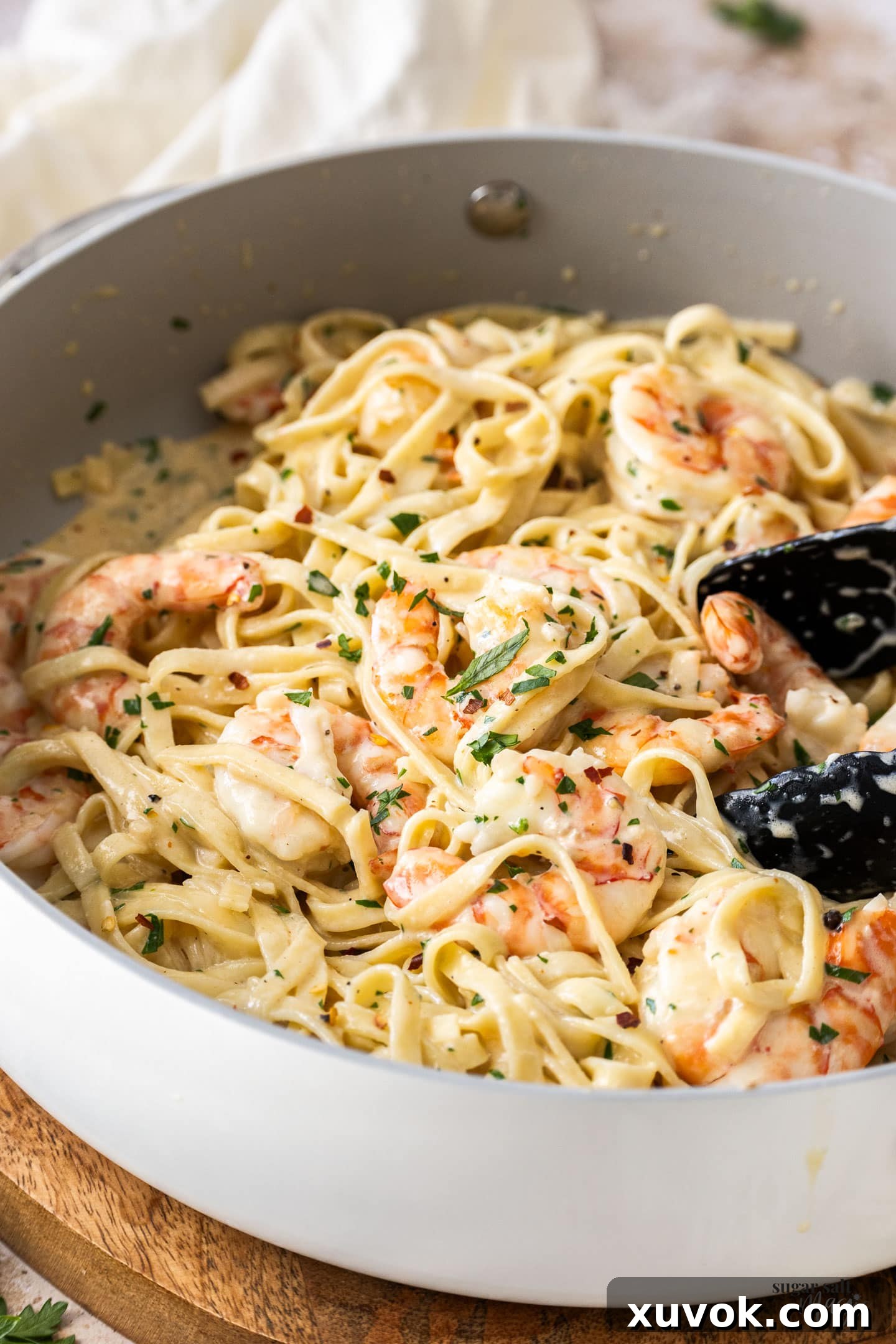 Prawns and creamy linguine being tossed in a pan with tongs, ready for serving.