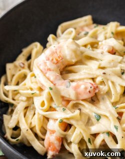 Super close up of a creamy prawn resting on a bed of linguine, ready to be eaten.