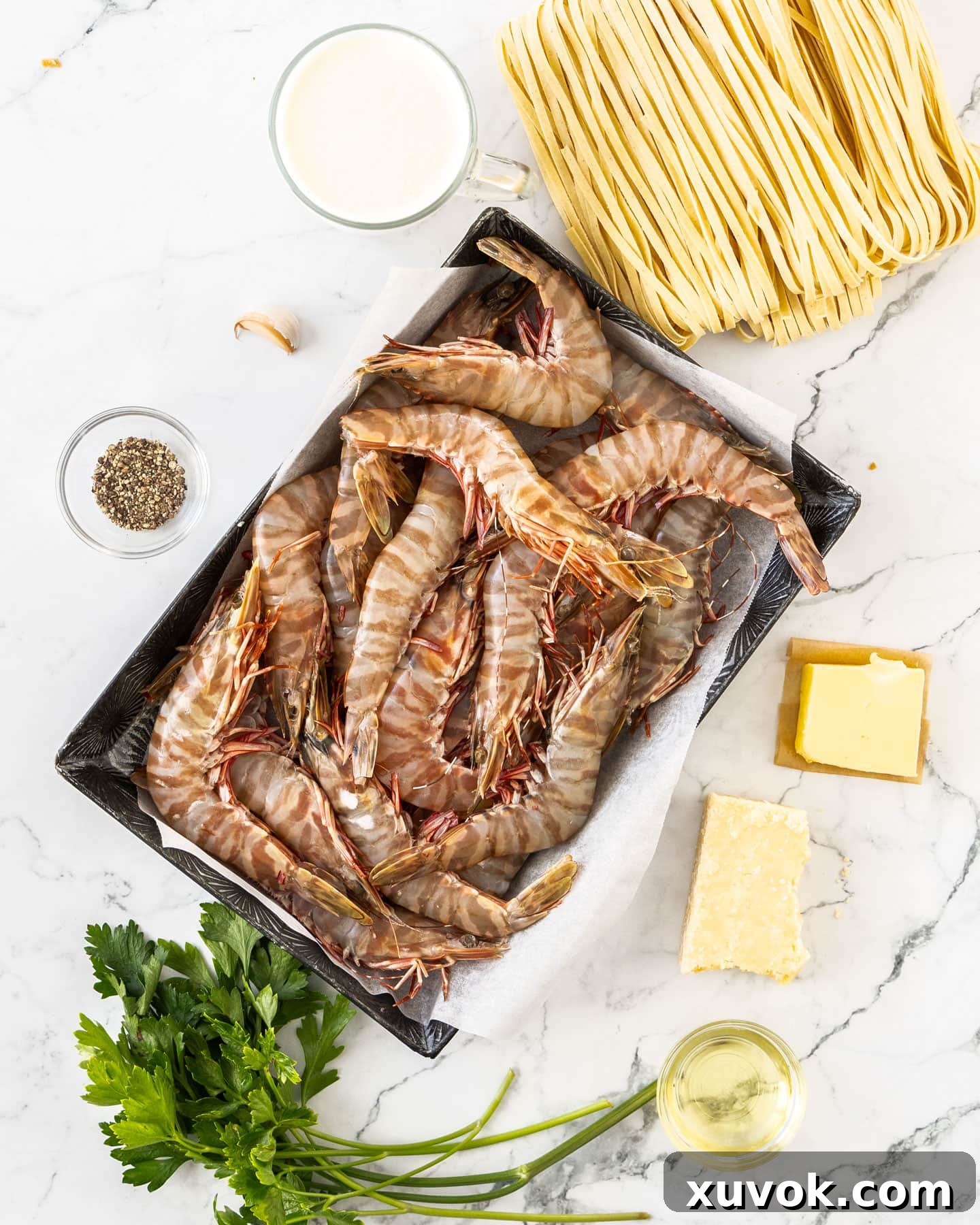 Fresh ingredients for creamy prawn linguine artfully arranged on a marble surface.