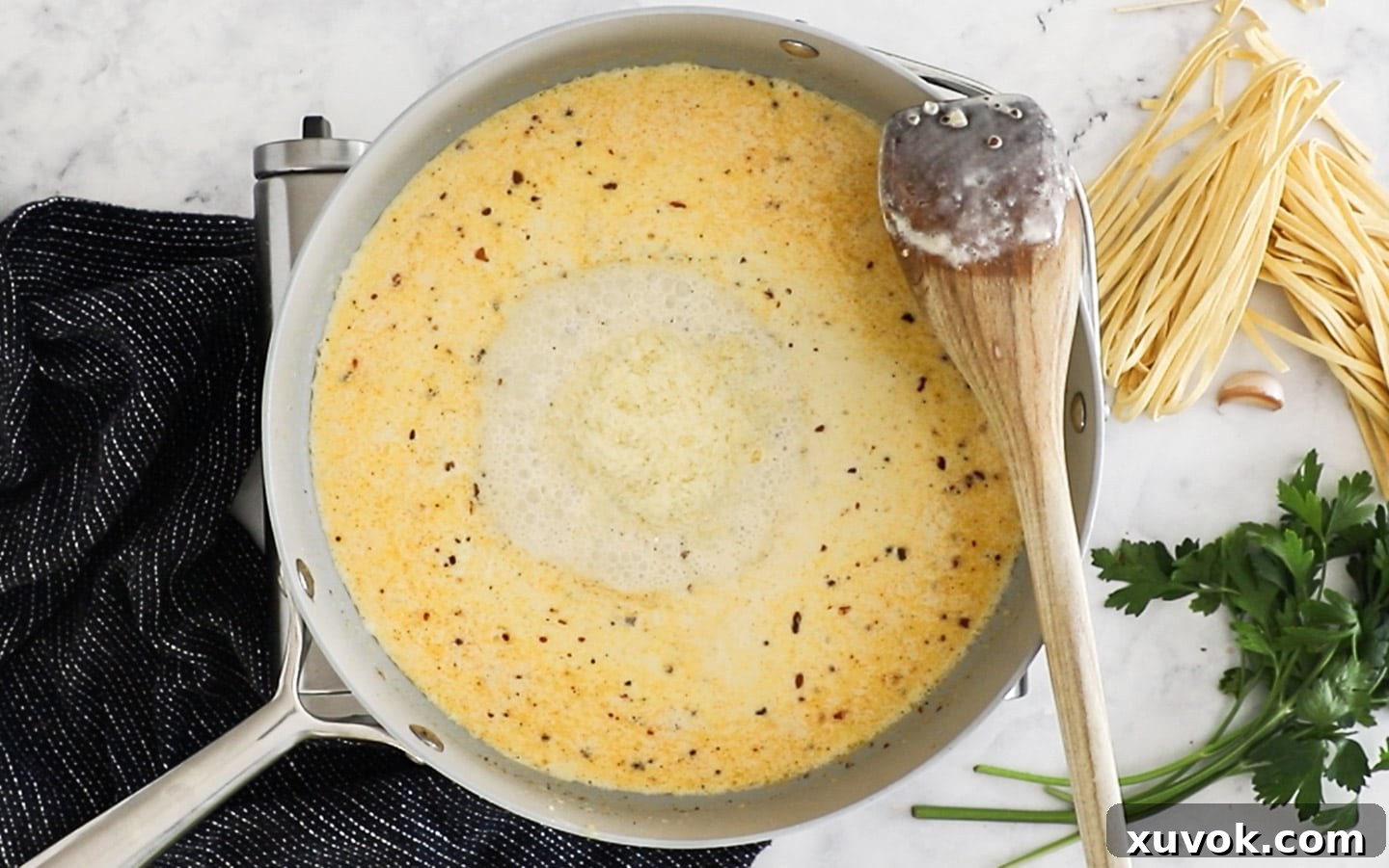 Finely grated Parmesan cheese being stirred into the creamy sauce in a pan.