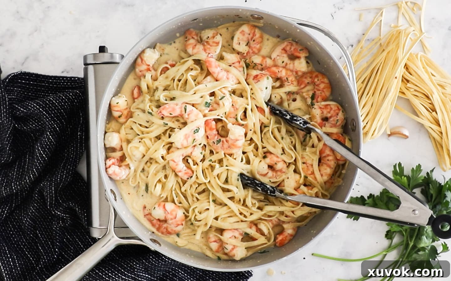 Cooked linguine, seared prawns, and fresh parsley mixed into the creamy sauce in a pan.
