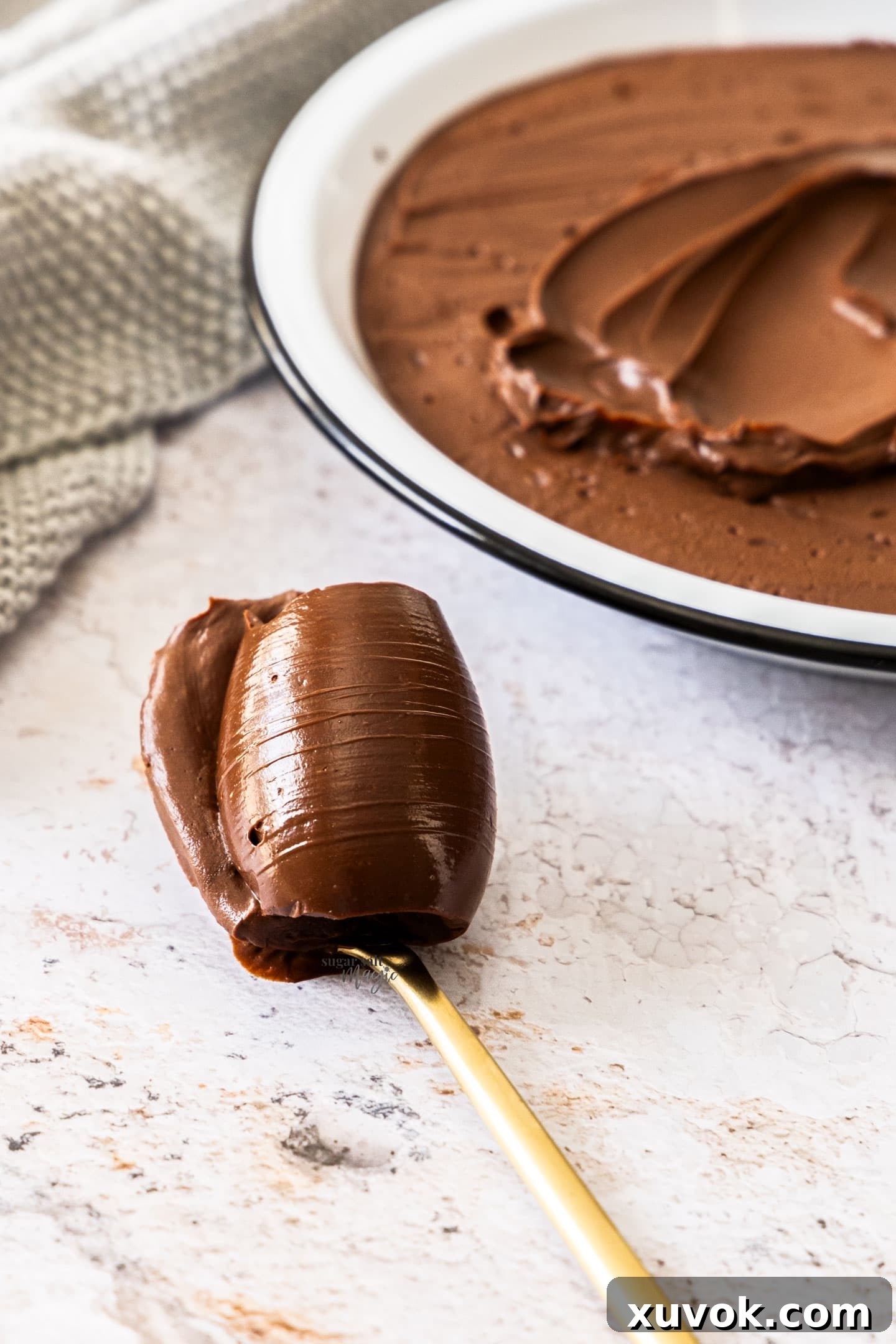 A spoon with a generous scoop of dark chocolate cremeux, highlighting its smooth, glossy, and indulgent texture.