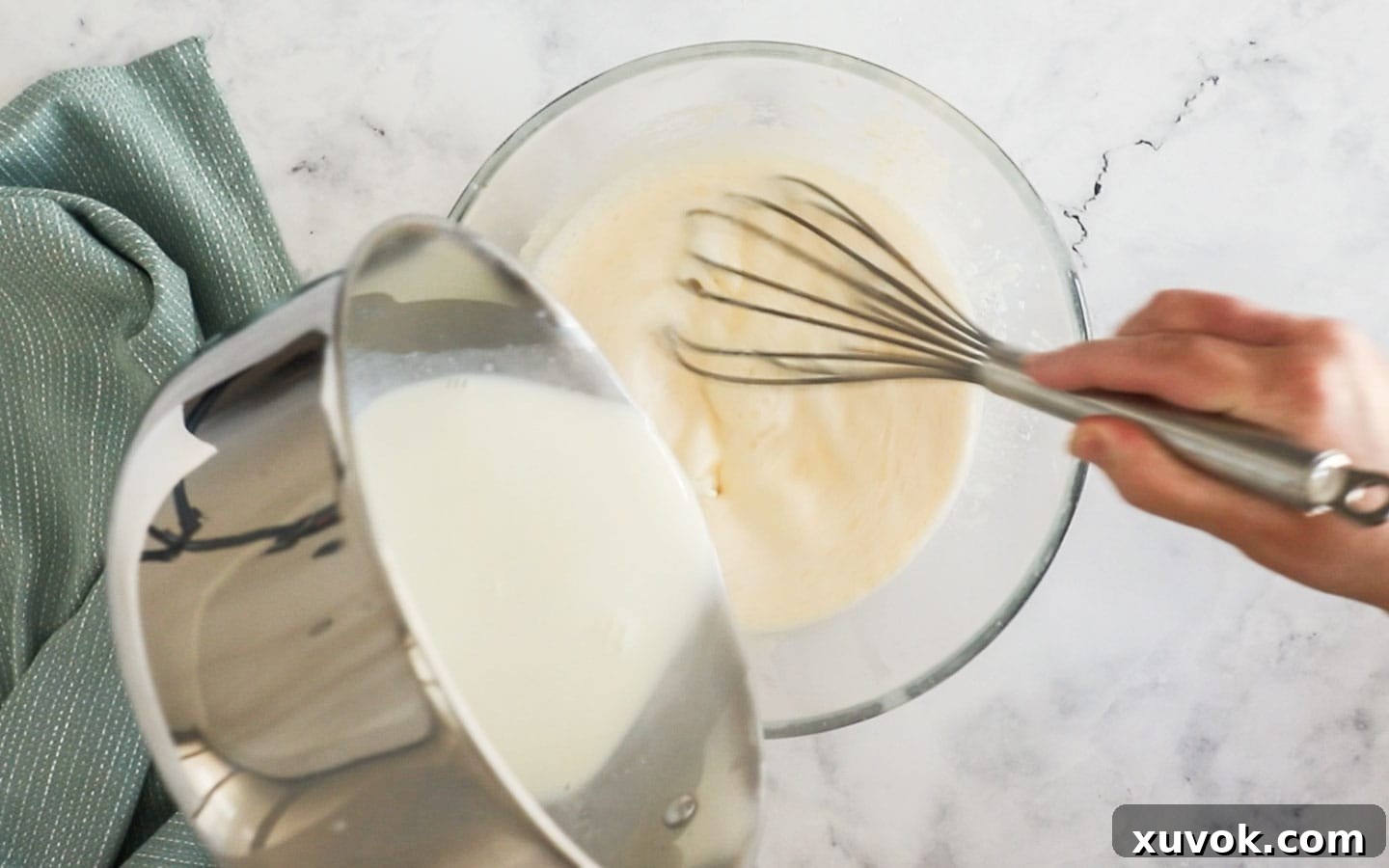 Adding hot milk mixture slowly to whisked eggs while continuously stirring to temper them.