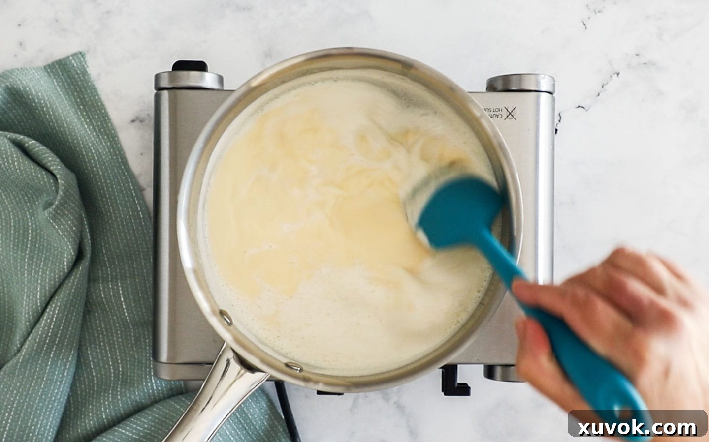 Stirring creme anglaise on the stovetop as it thickens to nappe consistency, showing diligent stirring.
