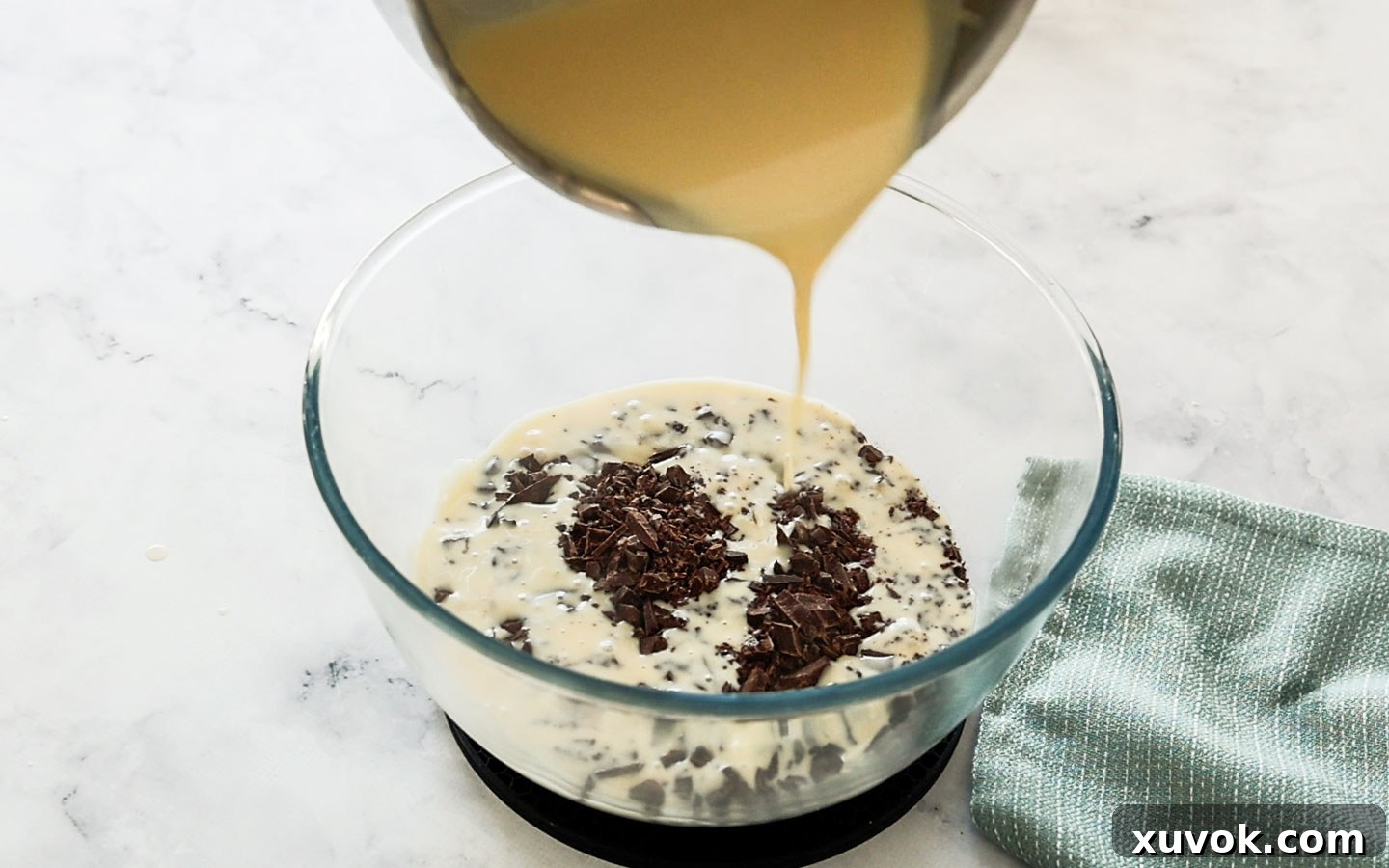 Pouring hot creme anglaise over finely chopped chocolate in a bowl, allowing the chocolate to melt.