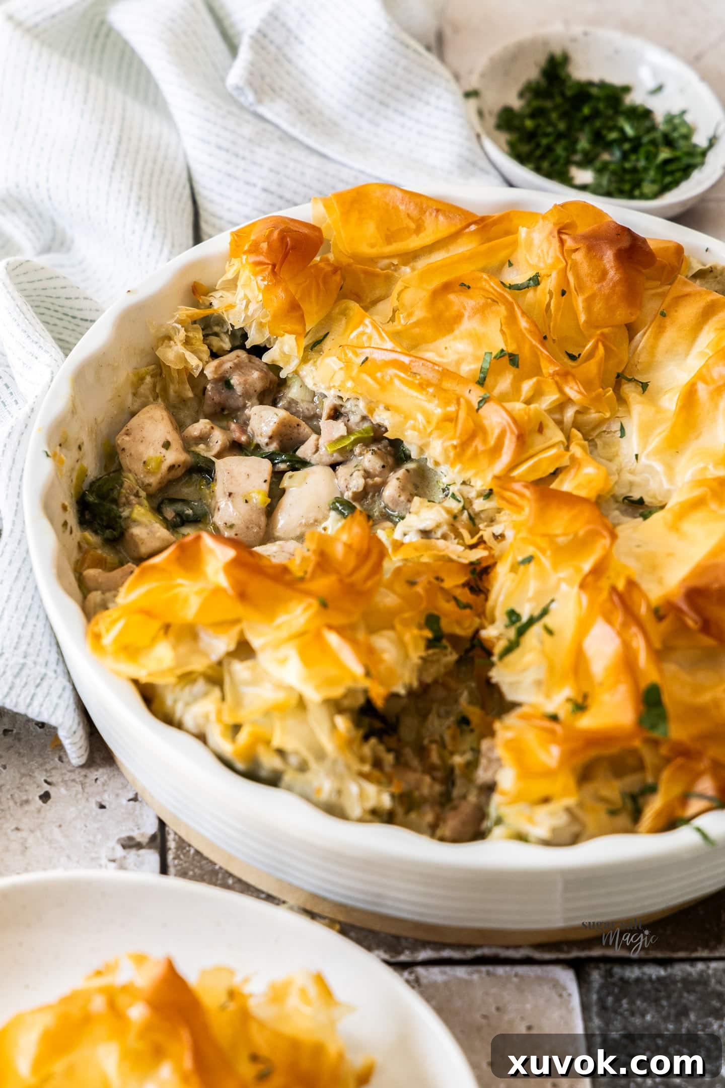 A golden-brown chicken filo pie with a slice cut out, revealing the rich, creamy chicken, leek, and bacon filling inside.