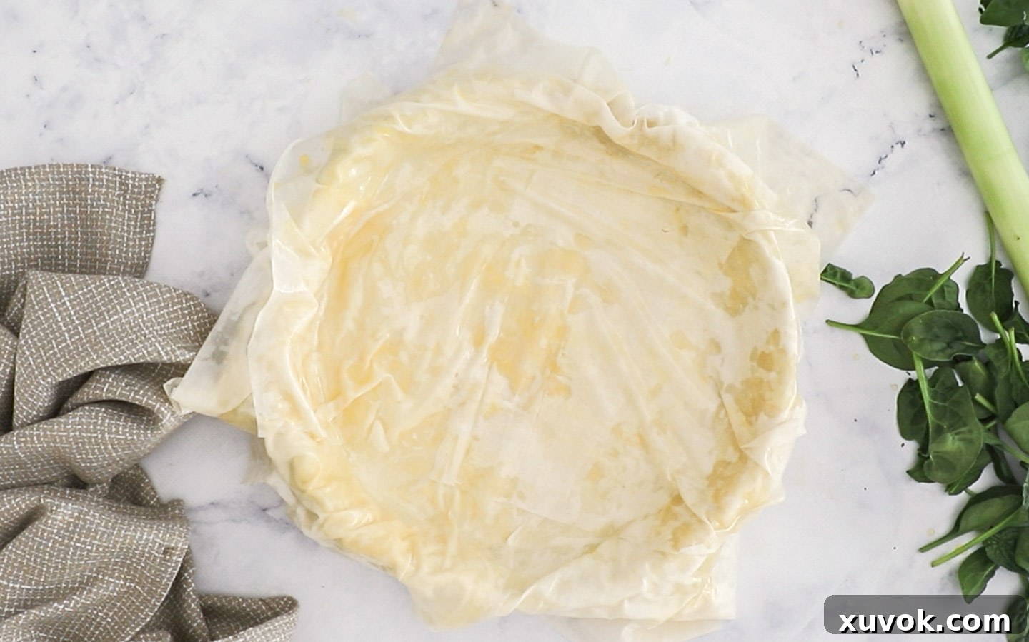 Multiple sheets of buttered filo pastry carefully layered and overlapping in a pie dish, creating the base.