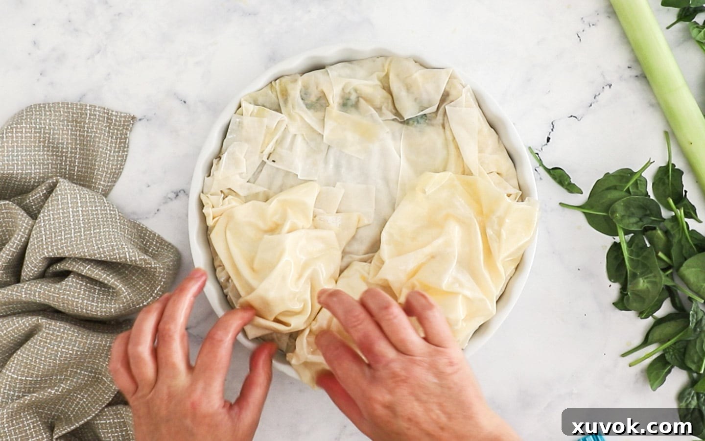 A sheet of filo pastry being scrunched up into a loose, buttery bundle, ready for the pie top.