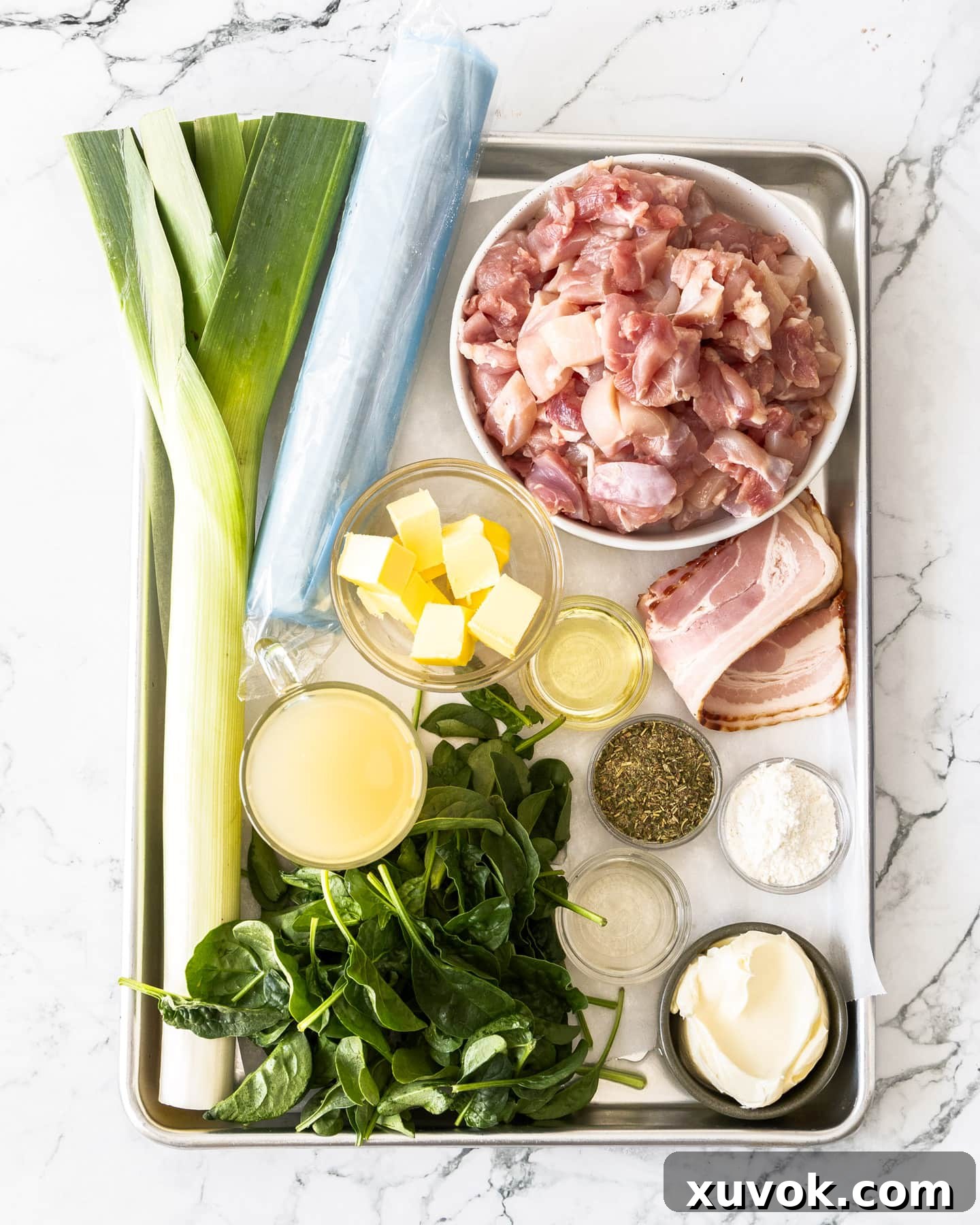 A flat lay image displaying all the fresh ingredients for chicken filo pie, including chicken thighs, leeks, bacon, spinach, butter, and filo pastry.