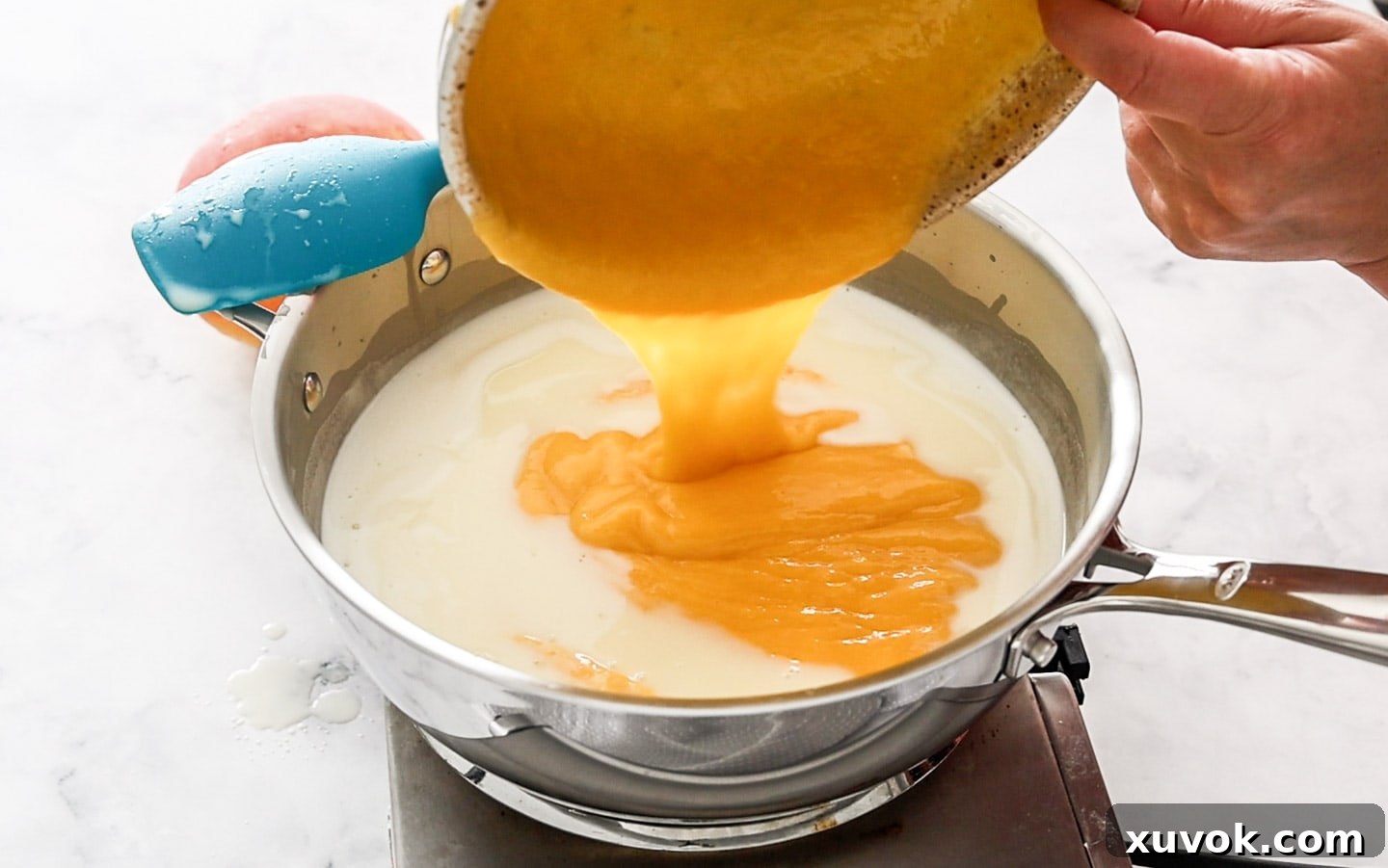 Adding mango puree to hot milk in a saucepan, being stirred.