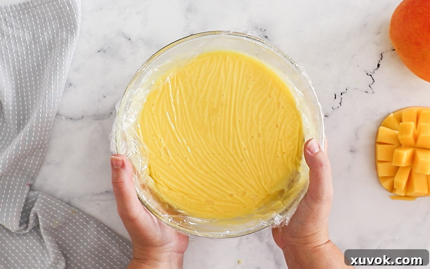 A bowl of mango custard covered with plastic wrap, pressed tightly to the surface.