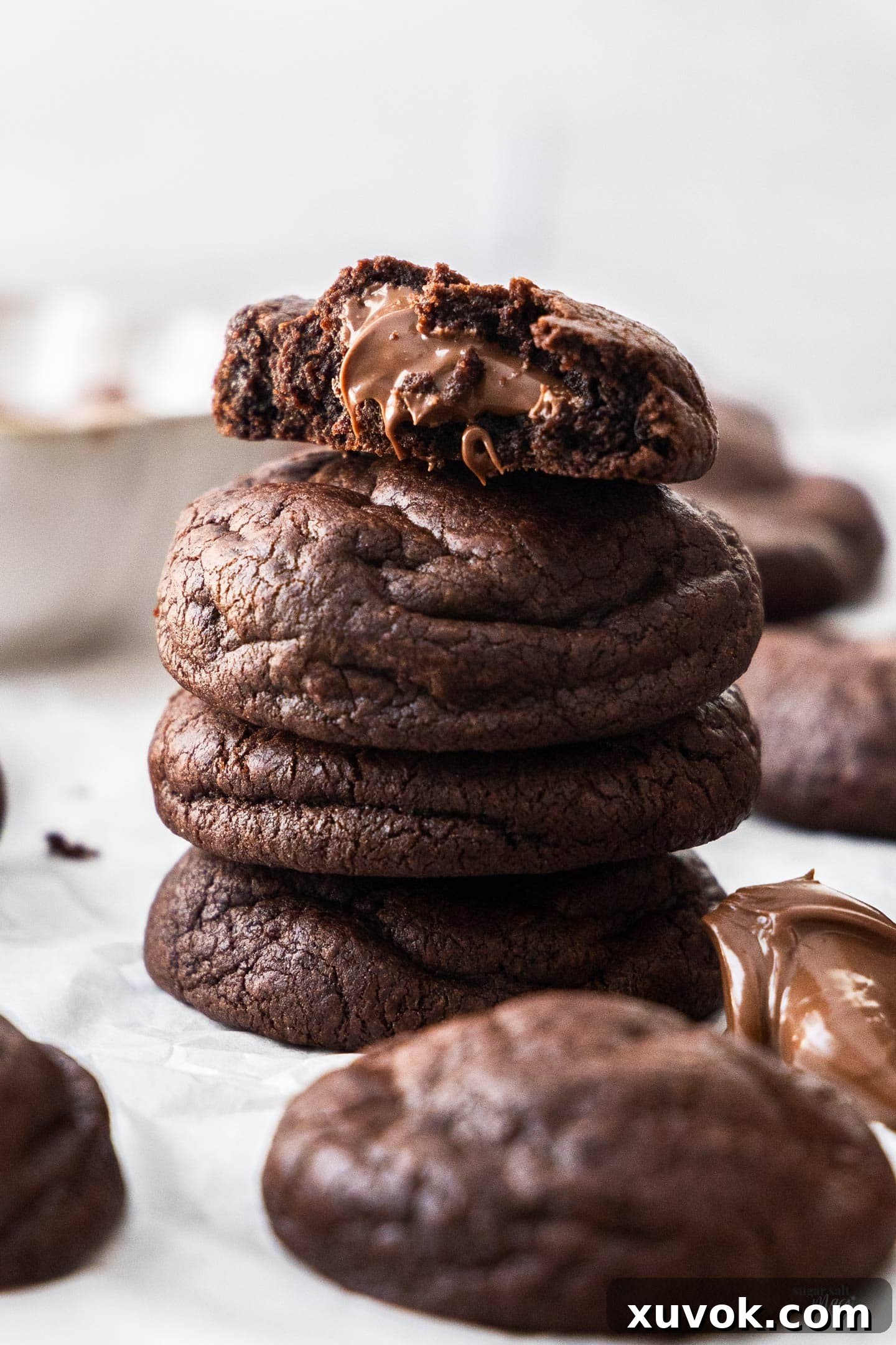 A stack of chocolate Nutella cookies with the top one broken open to show the gooey middle.