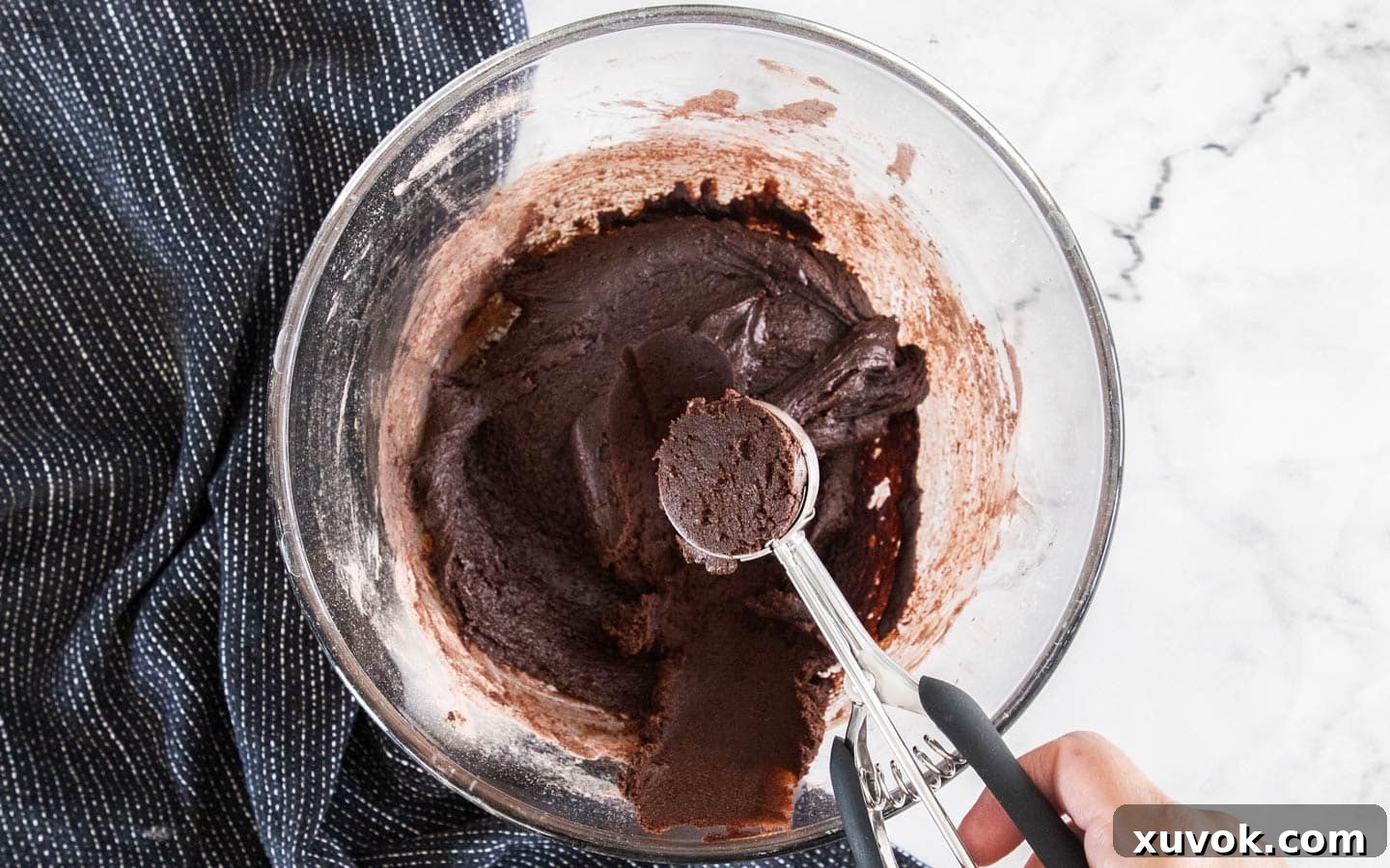 Using a cookie scoop to scoop the cookie dough out of the bowl.