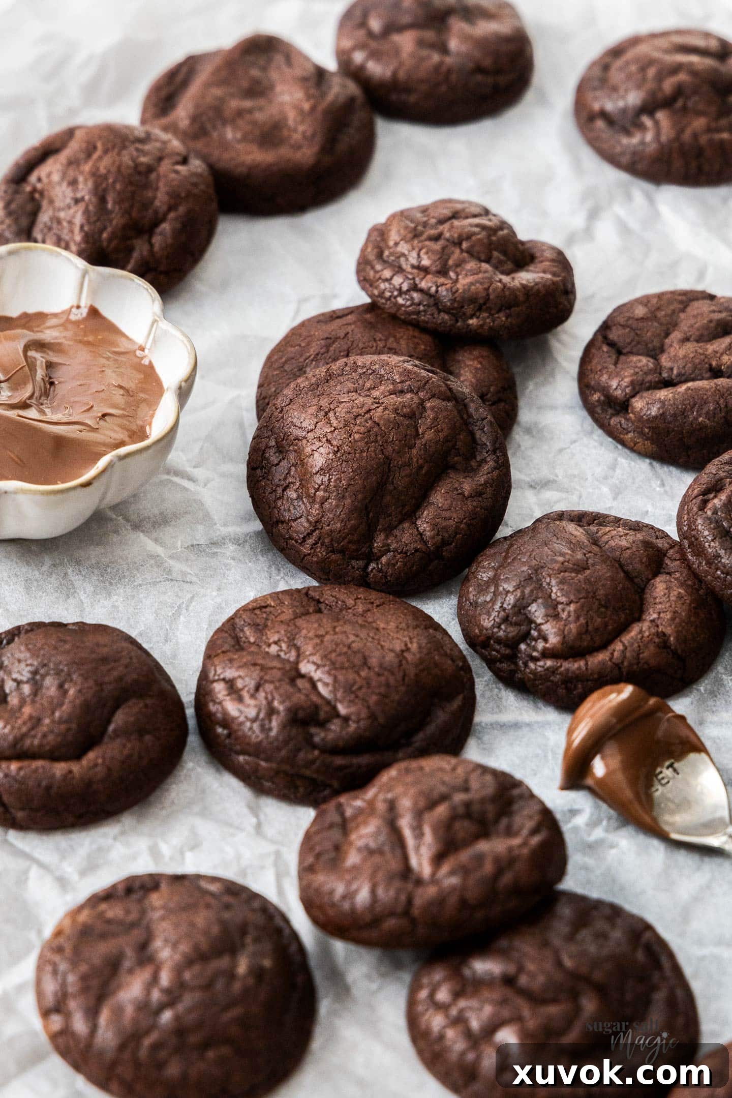 A batch of baked chocolate Nutella cookies with a little bowl of Nutella next to them.