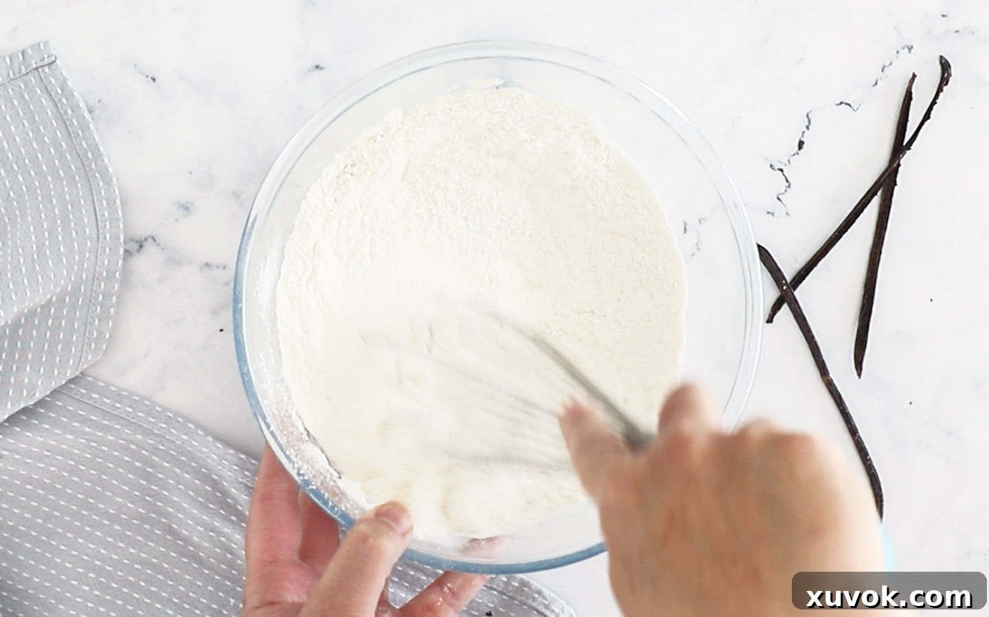 Close-up of a whisk blending flour, baking powder, sugar, and salt in a bowl.